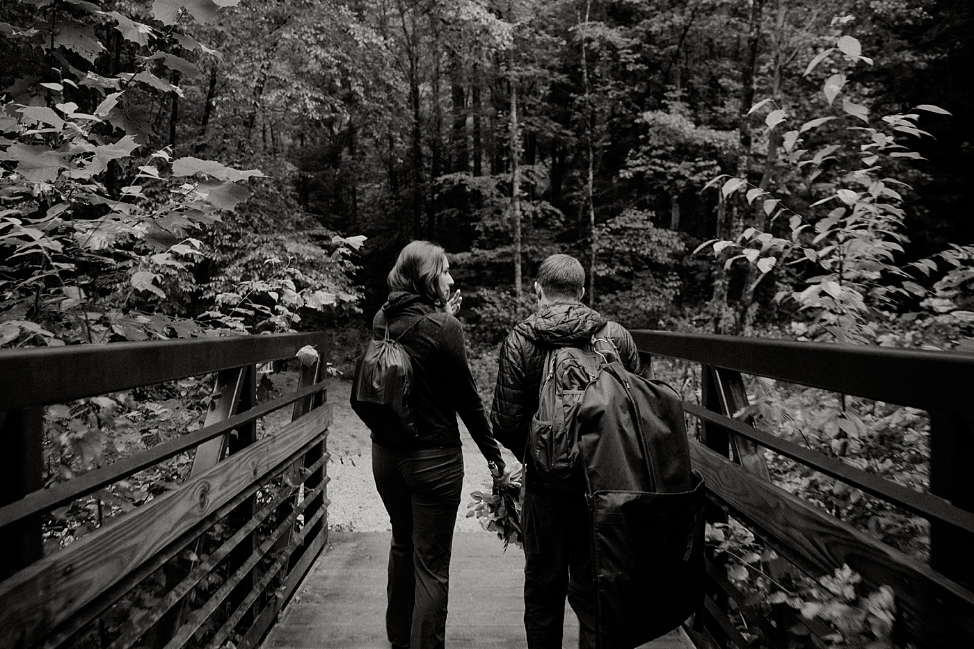 B&W of Bride and Groom in hiking gear on forest bridge Catawba Falls Asheville, NC Elopement Photography captured by Maggie Alvarez Photography