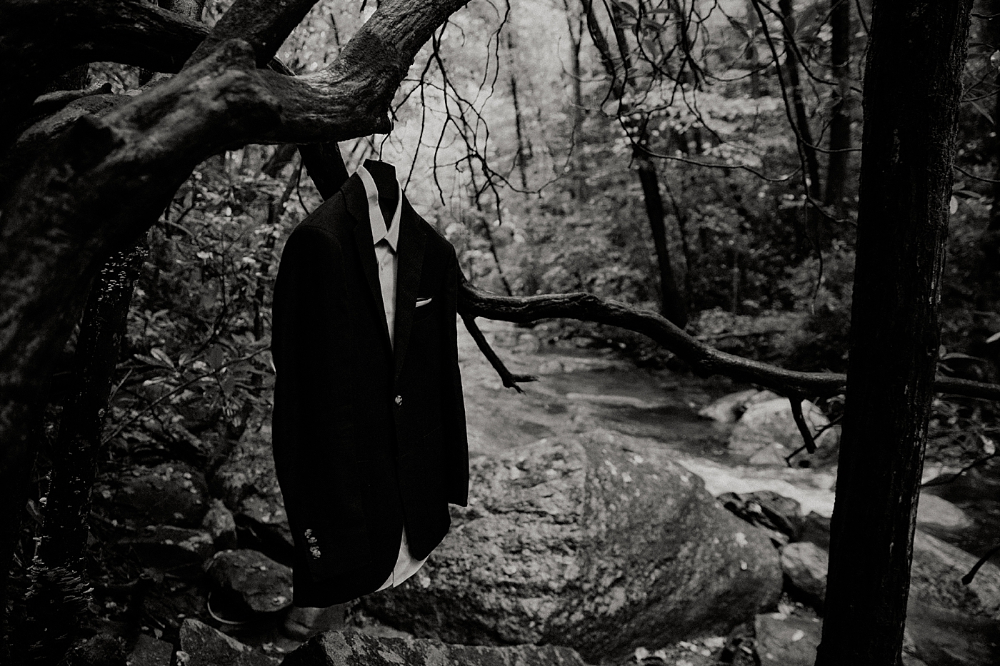 Black and white detail shot of suit on coat hanger on tree in the forest Catawba Falls Asheville, NC Elopement Photography captured by Maggie Alvarez Photography
