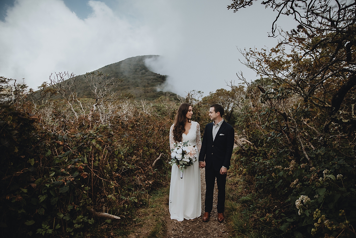 Bride and groom holding hands with foggy mountain behind them Catawba Falls Asheville, NC Elopement Photography captured by Maggie Alvarez Photography
