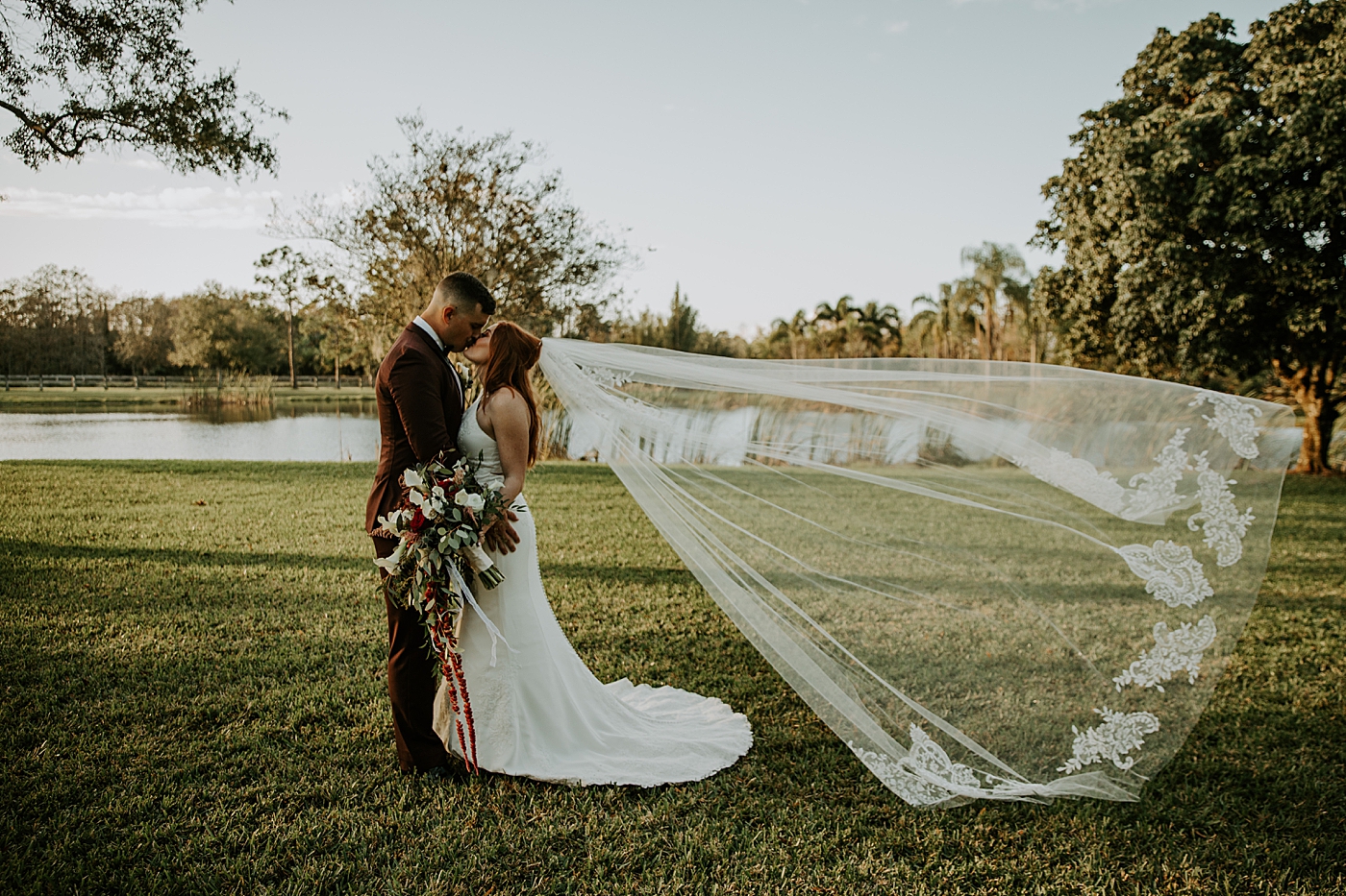 Bride and Groom kissing with veil flowing in the wind Bride entering ceremony with father BMR Stables Wedding Photography captured by South Florida Wedding Photographer Maggie Alvarez Photography