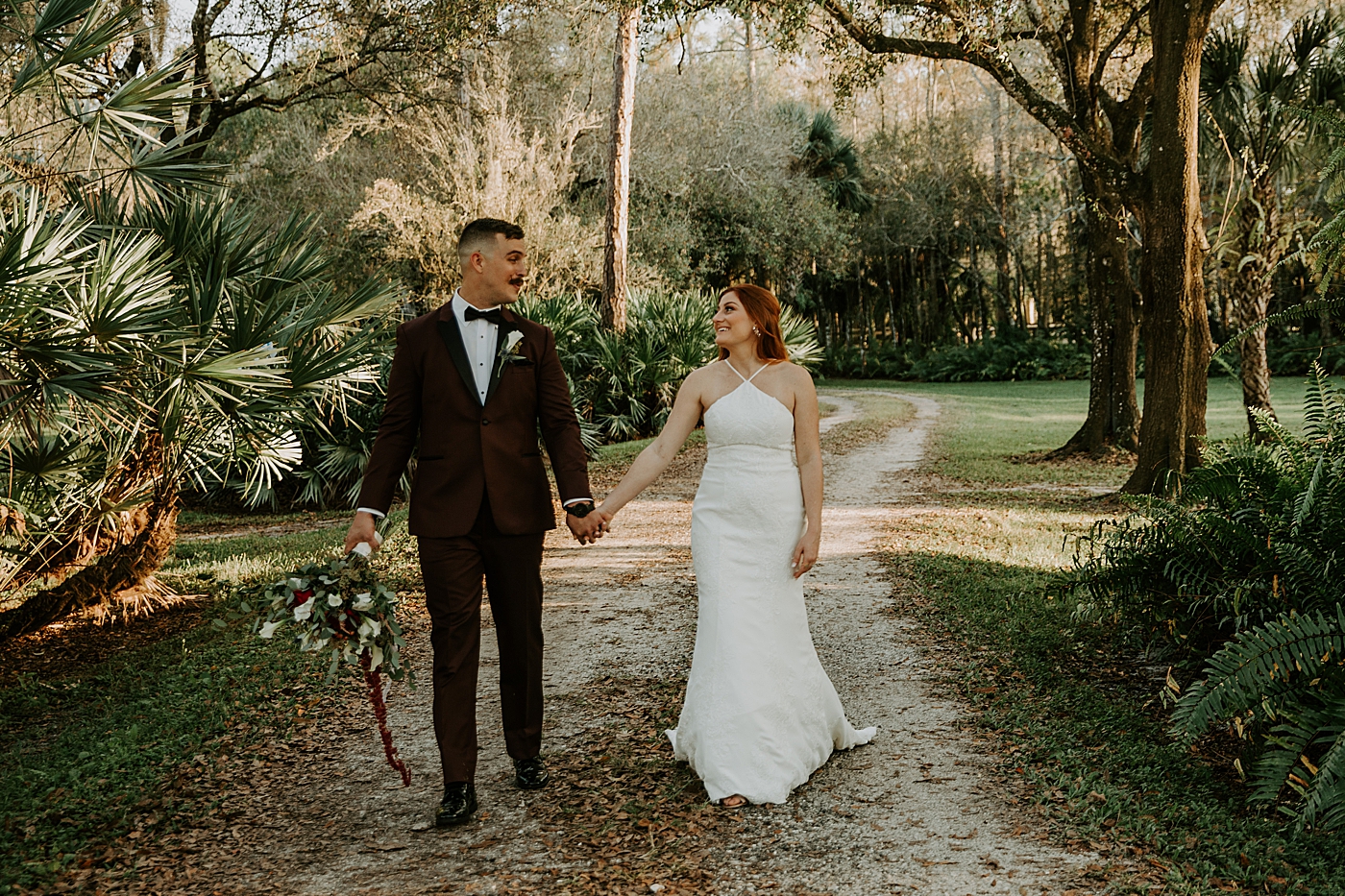 Bride and groom walking down a path as Groom holds bouquet Bride entering ceremony with father BMR Stables Wedding Photography captured by South Florida Wedding Photographer Maggie Alvarez Photography
