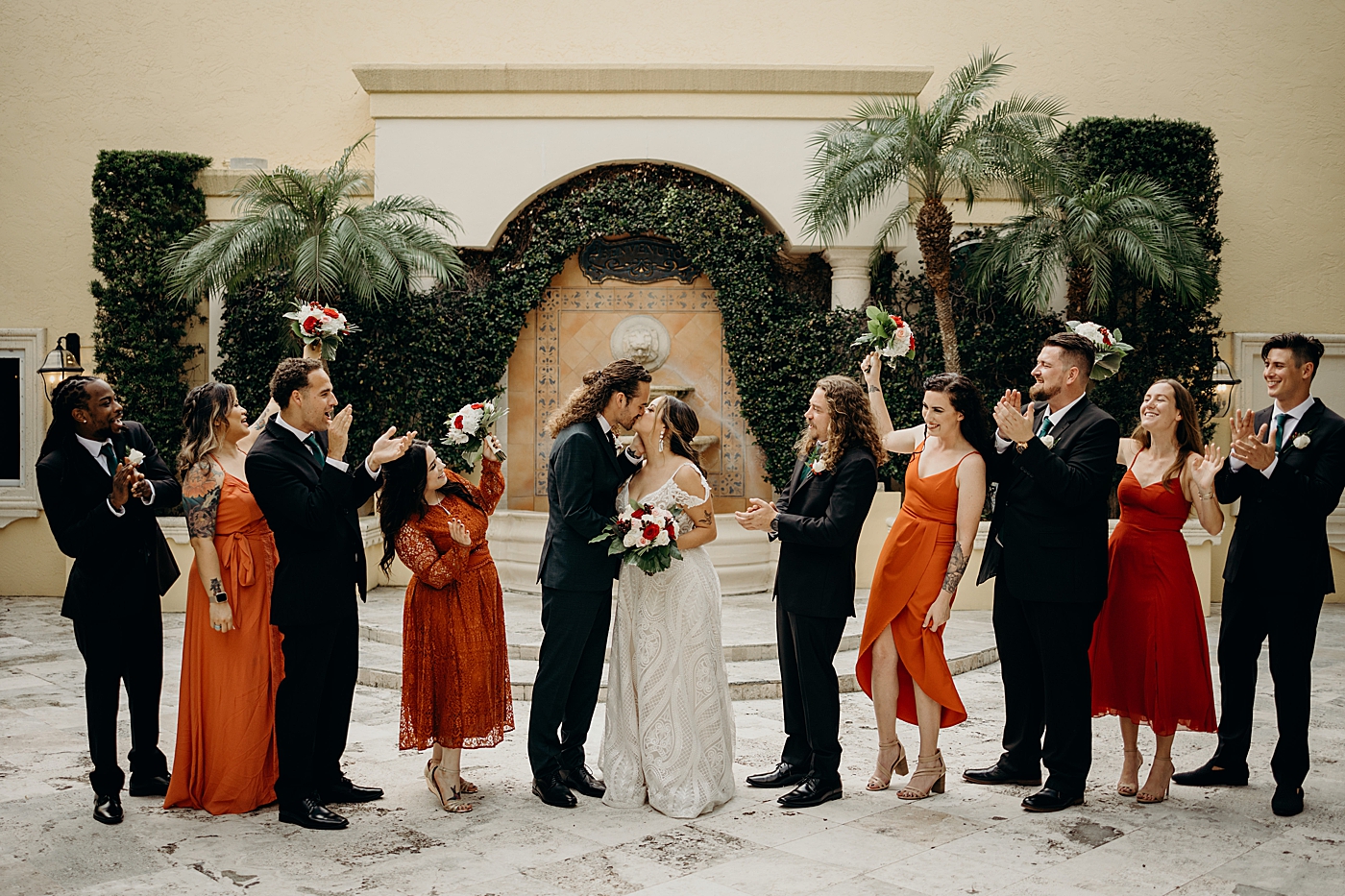 Groom and Bride kissing with Wedding Party celebrating Benvenuto Restaurant Wedding Photography captured by South Florida Wedding Photographer Maggie Alvarez Photography