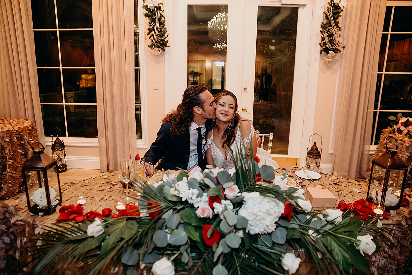 Bride and Groom sitting and the sweetheart table Groom kissing Bride Benvenuto Restaurant Wedding Photography captured by South Florida Wedding Photographer Maggie Alvarez Photography