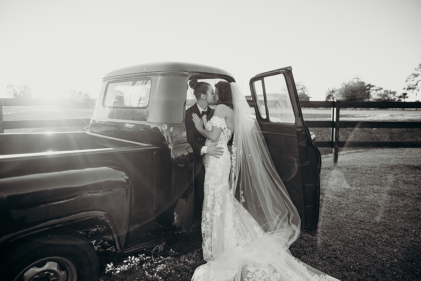 Brides kissing as one sits in classic truck black and white Ever After Farms Wedding Photography captured by South Florida Wedding Photographer Maggie Alvarez Photography