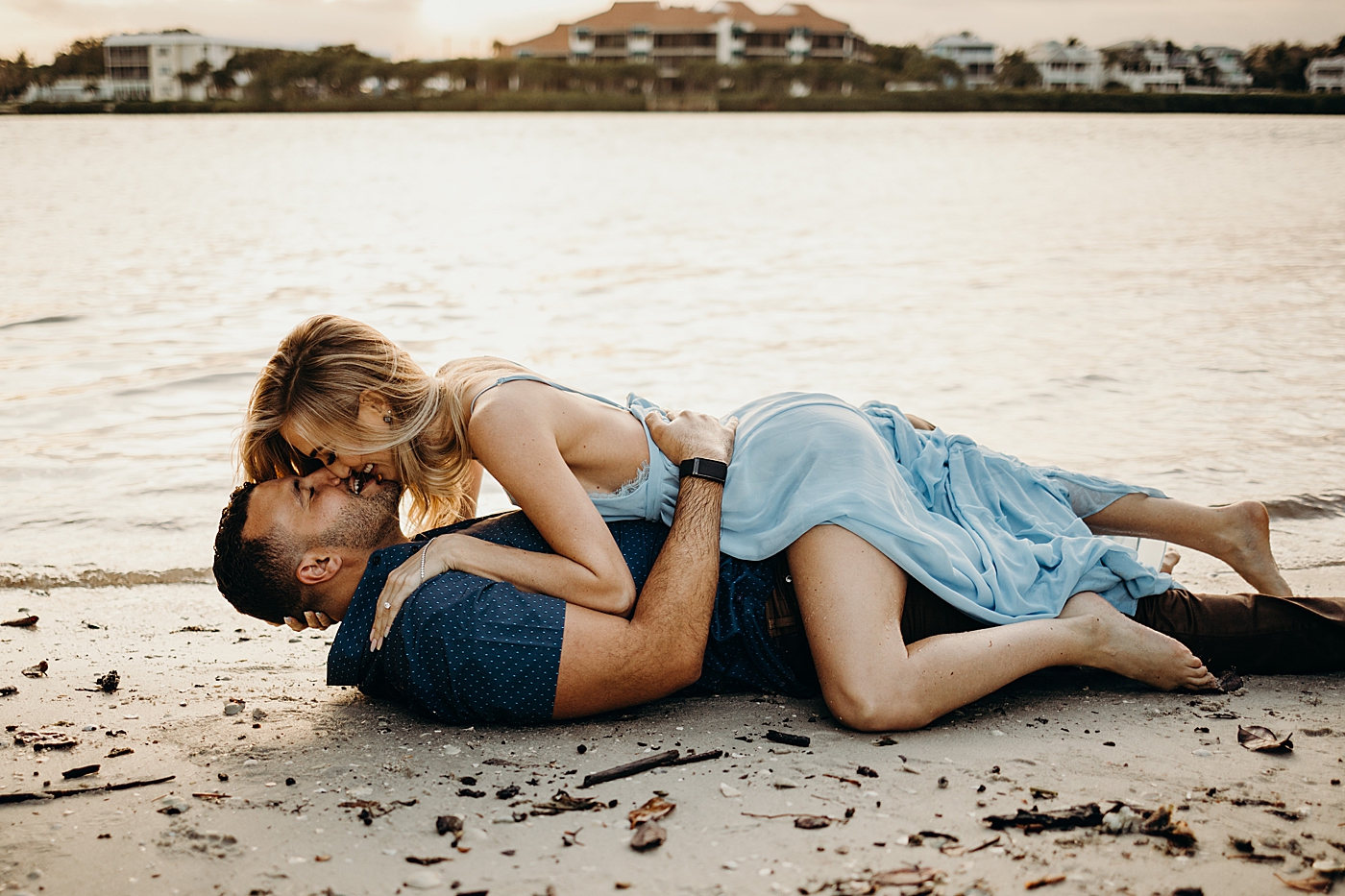 Woman on top of man on beach shore kissing Coral Cove Park Engagement Photography captured by Maggie Alvarez Photography