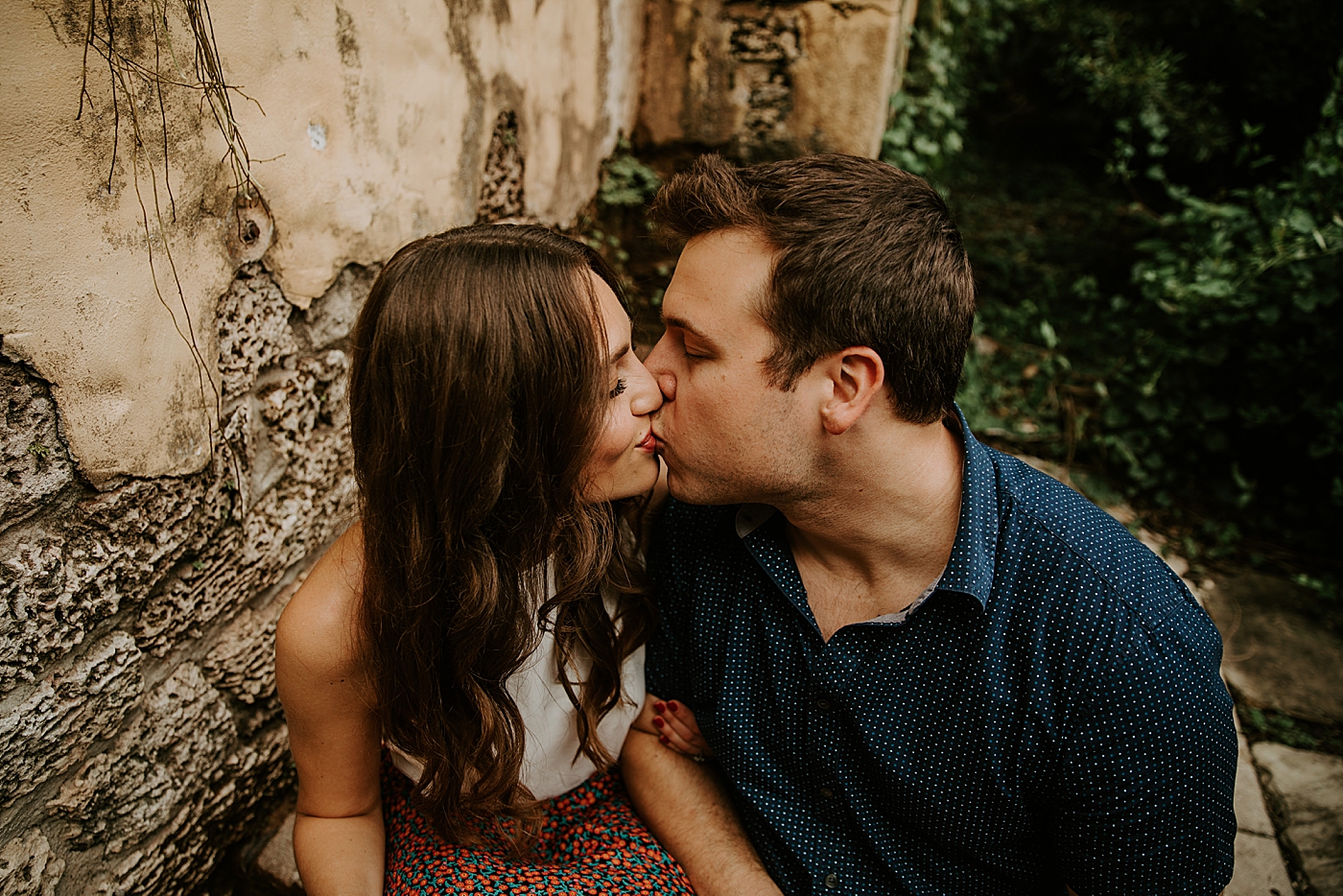 Couple sitting by wall and kissing each other Deering Estate Engagement Photography captured by Maggie Alvarez Photography