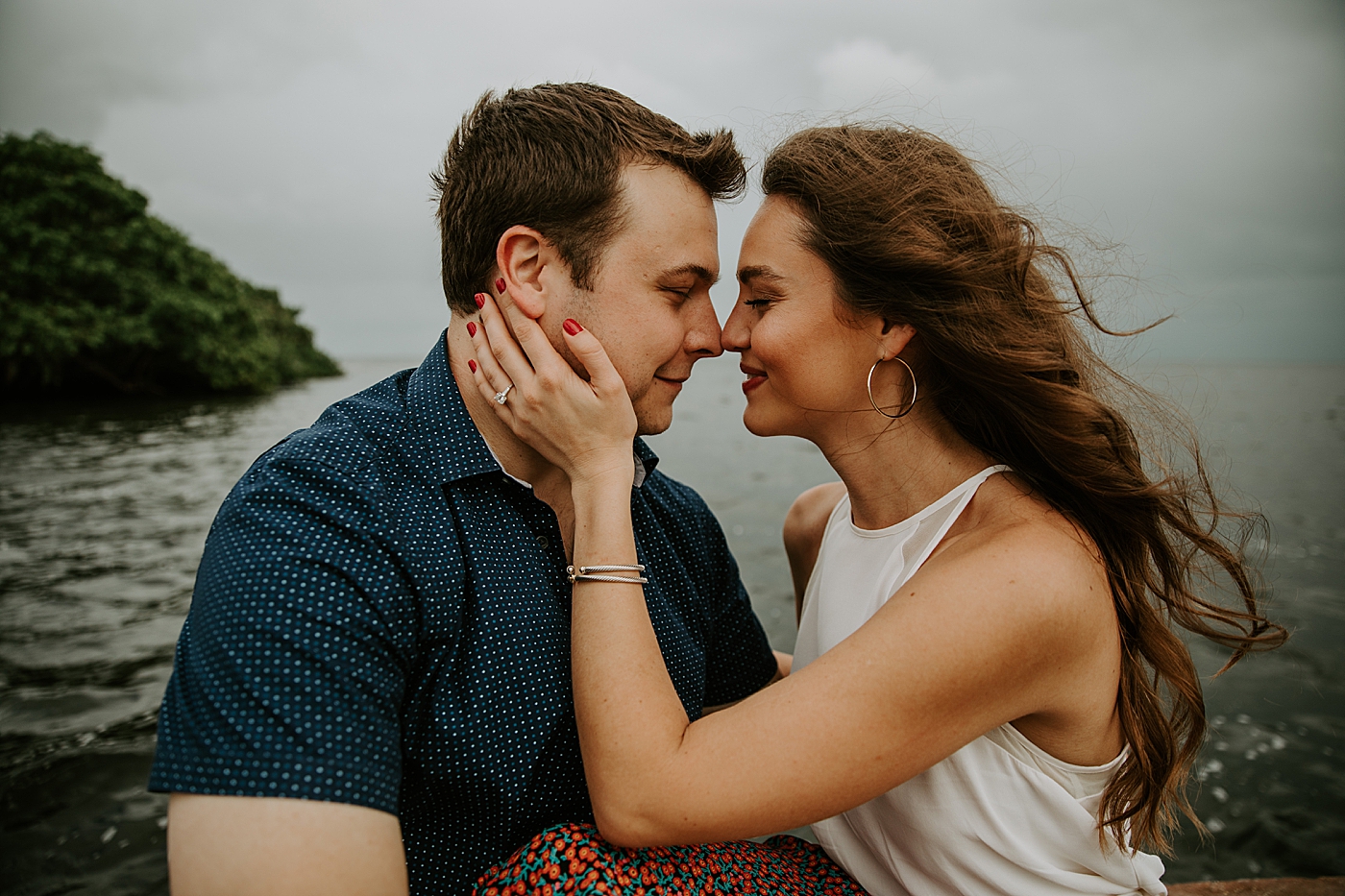 Lady holding man's face with calm lake behind them Deering Estate Engagement Photography captured by Maggie Alvarez Photography