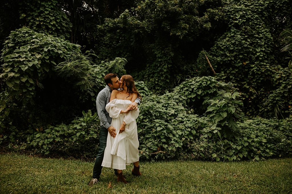 Couple kissing in front of green bushes Deering Estate Engagement Photography captured by Maggie Alvarez Photography