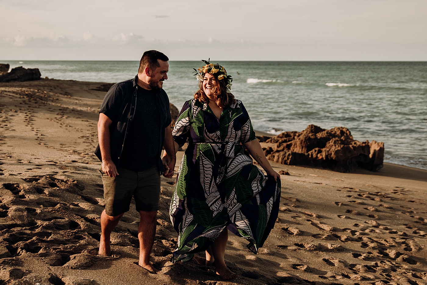 Couple holding hands walking on the sand with calm ocean House of Refuge Engagement Photography captured by Maggie Alvarez Photography