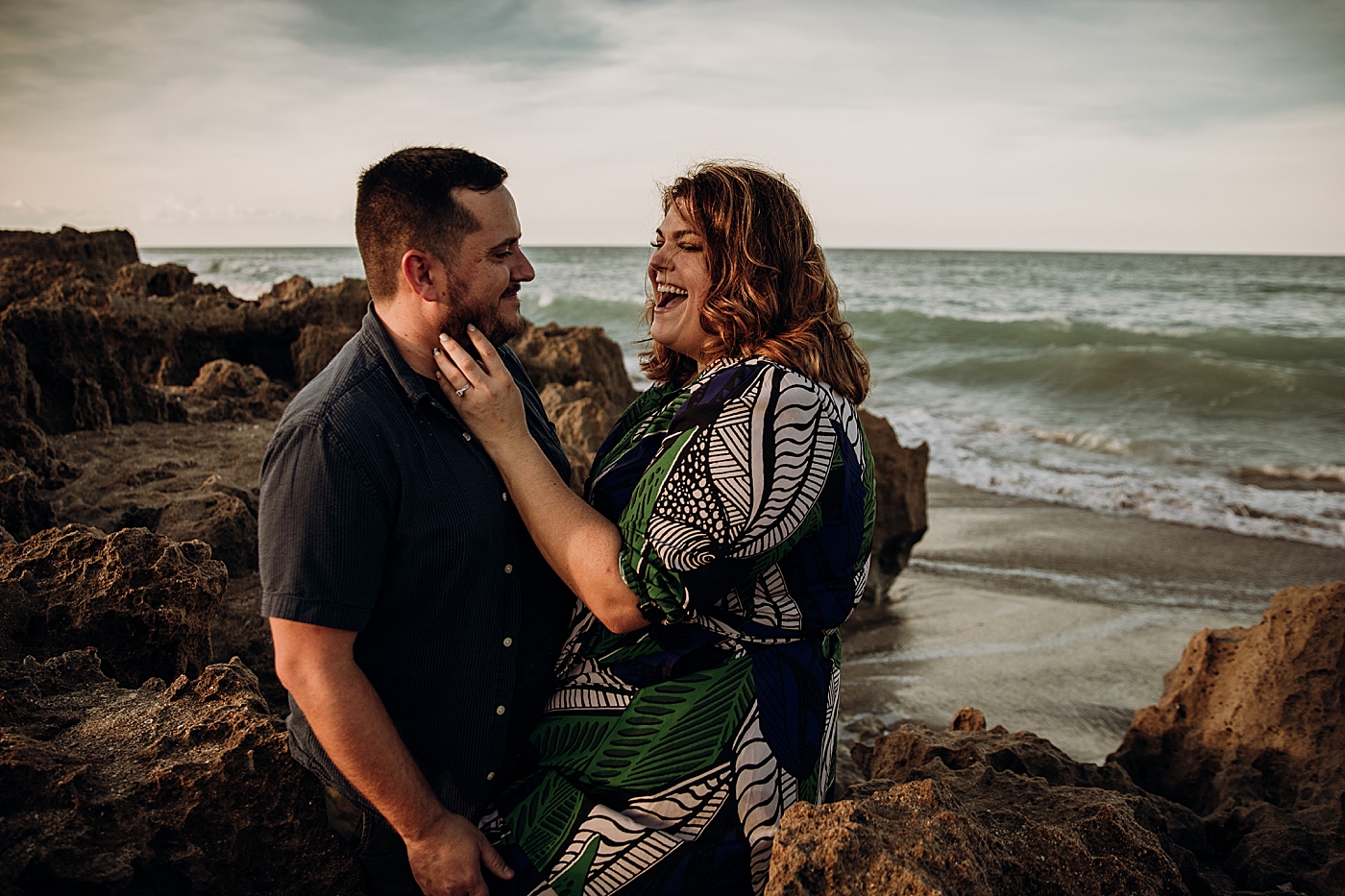 Couple resting on beach boulders with waves coming in House of Refuge Engagement Photography captured by Maggie Alvarez Photography