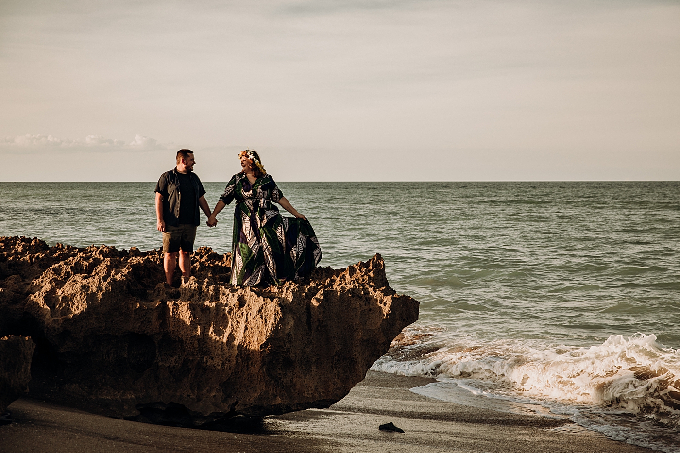 Couple standing on rock on the beach with calm ocean House of Refuge Engagement Photography captured by Maggie Alvarez Photography