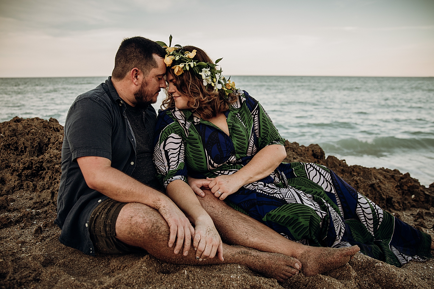 Couple resting and nuzzling on sandy rock by the ocean House of Refuge Engagement Photography captured by Maggie Alvarez Photography
