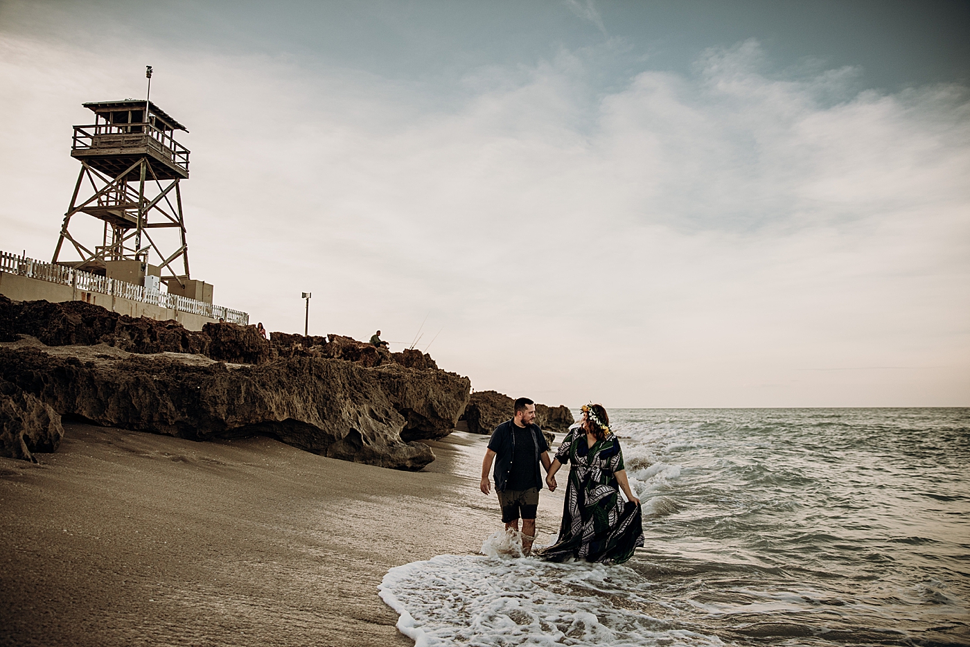 Couple walking on the beach as waves come in House of Refuge Engagement Photography captured by Maggie Alvarez Photography