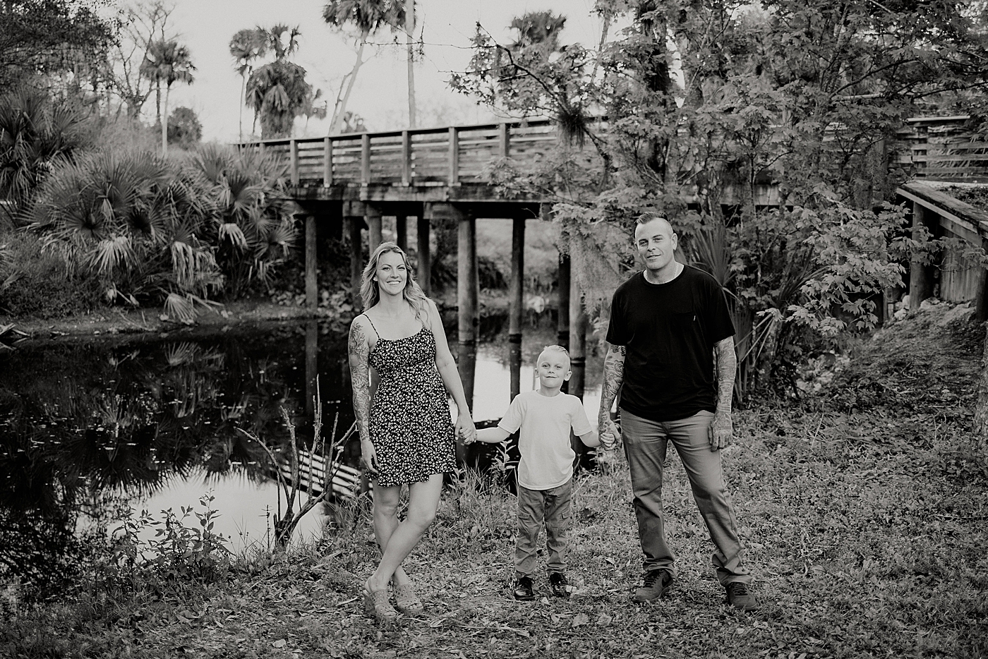 B&W Family holding hands and standing by calm water Park Family Photography by South Florida Family Photographer Maggie Alvarez Photography