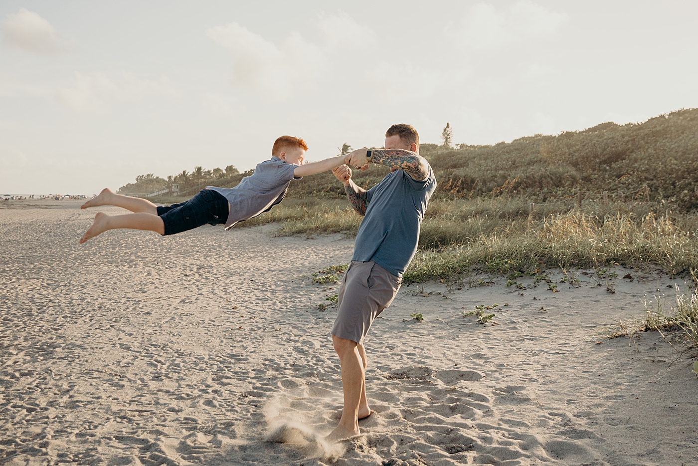 Dad swinging son by the arms in the air on the beach Ocean Ridge Hammock Park Family Photography by South Florida Family Photographer Maggie Alvarez Photography