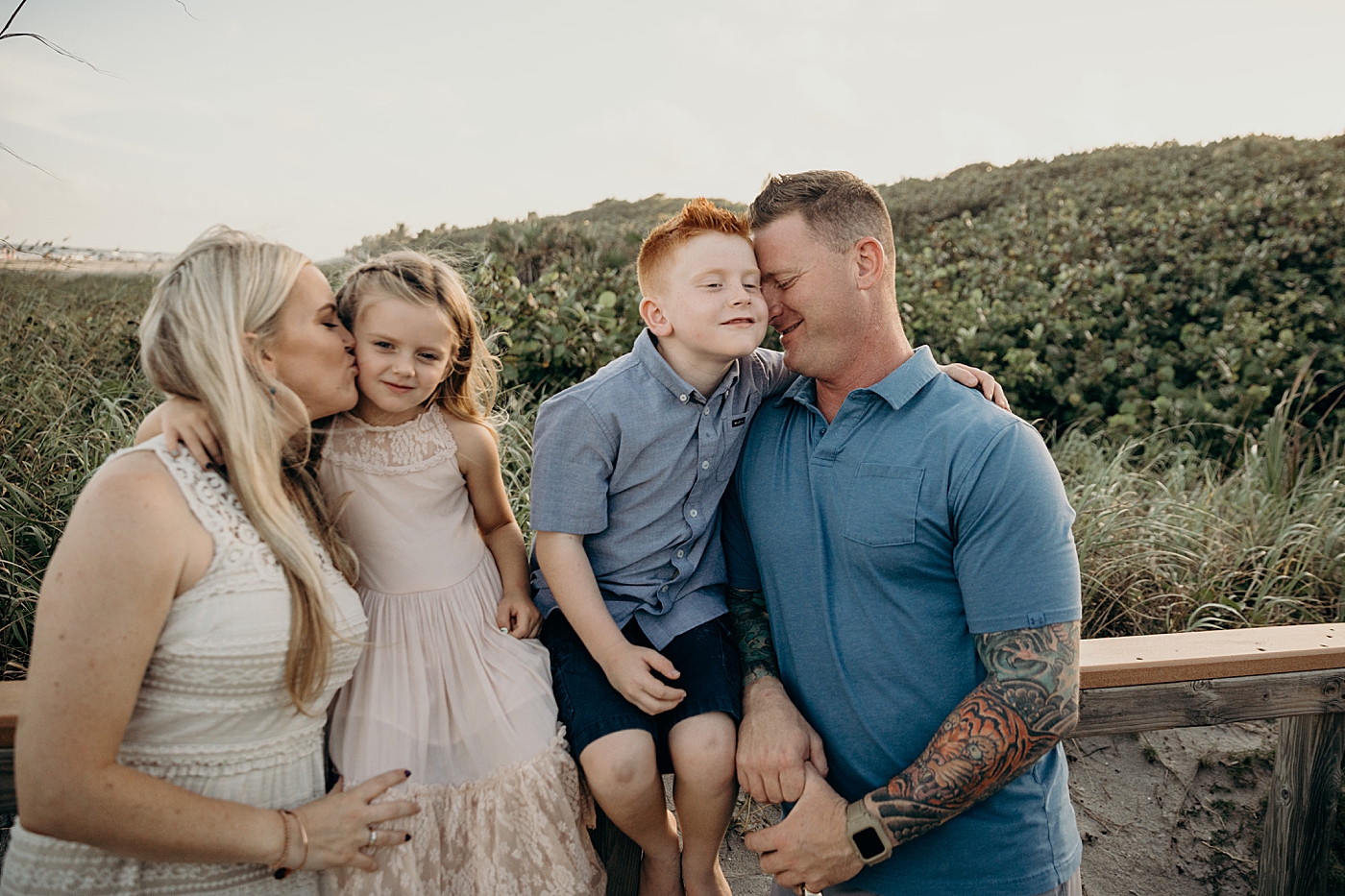 Mother kissing daughter on the cheek and father holding son close nuzzling Ocean Ridge Hammock Park Family Photography by South Florida Family Photographer Maggie Alvarez Photography