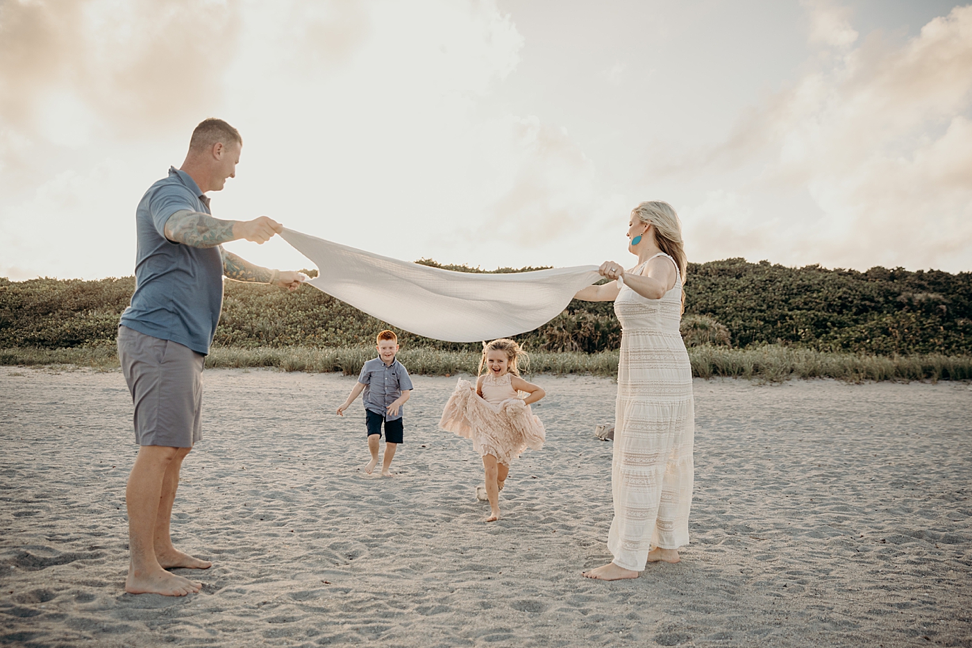 Parent's holding up beach towel as children running underneath Ocean Ridge Hammock Park Family Photography by South Florida Family Photographer Maggie Alvarez Photography