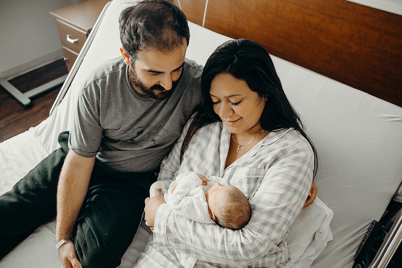 Parents in hospital bed together with Mother holding baby in her arms South Florida Fresh 48 Newborn Photography by South Florida Family Photographer Maggie Alvarez Photography