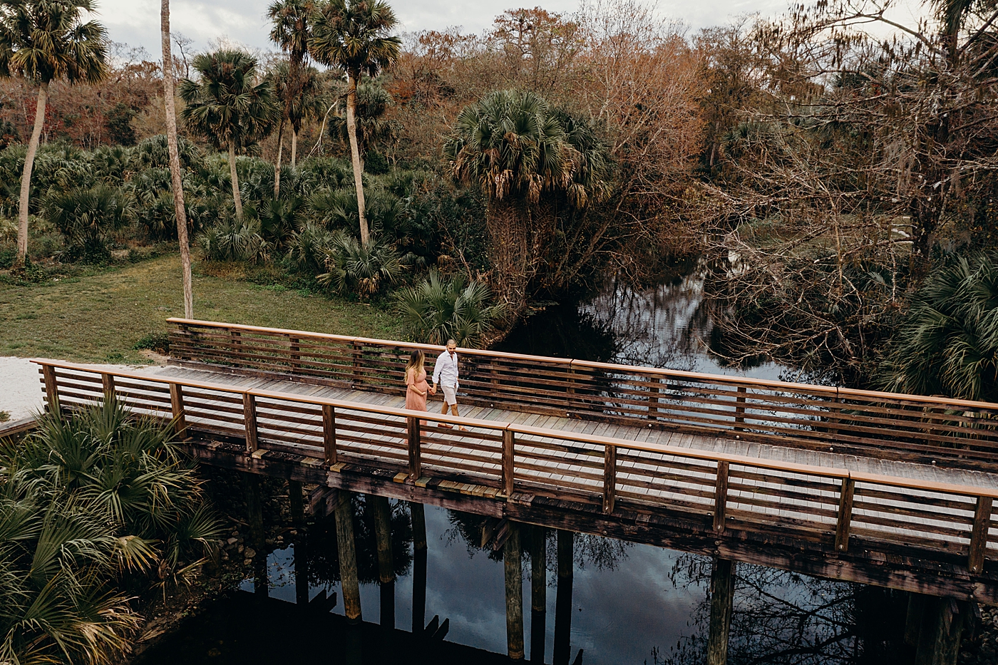 Wide shot of couple crossing the bridge holding hands Riverbend Park Maternity Photography by South Florida Family Photographer Maggie Alvarez Photography