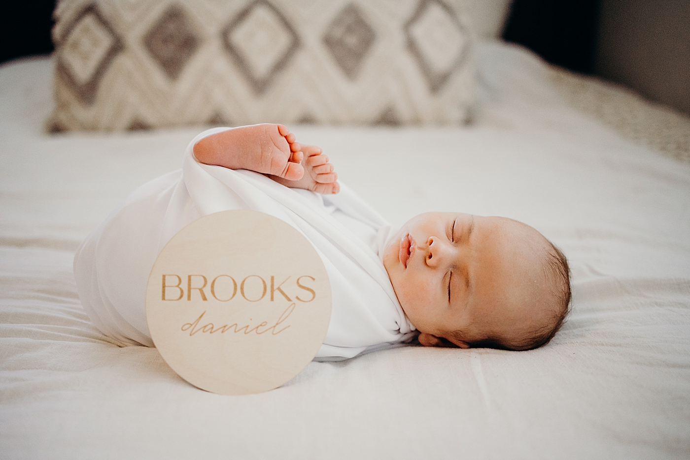 Baby sleeping in swaddle on bed with circle name sign South Florida Newborn Photography captured by South Florida Family Photographer Maggie Alvarez Photography