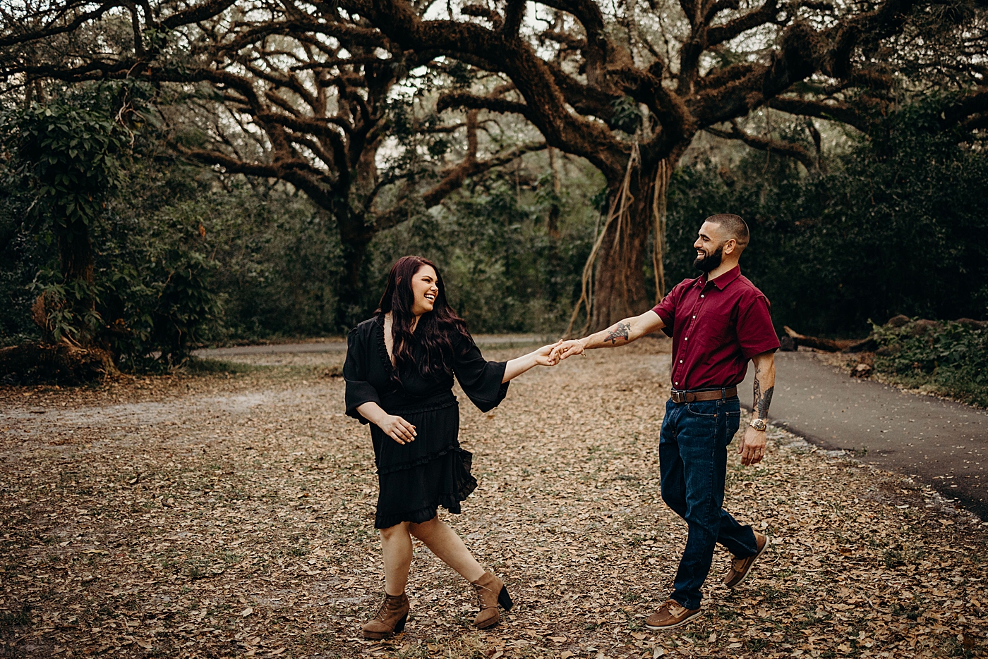 Woman leading man through fall forest Tree Top Park Engagement Photography captured by Maggie Alvarez Photography