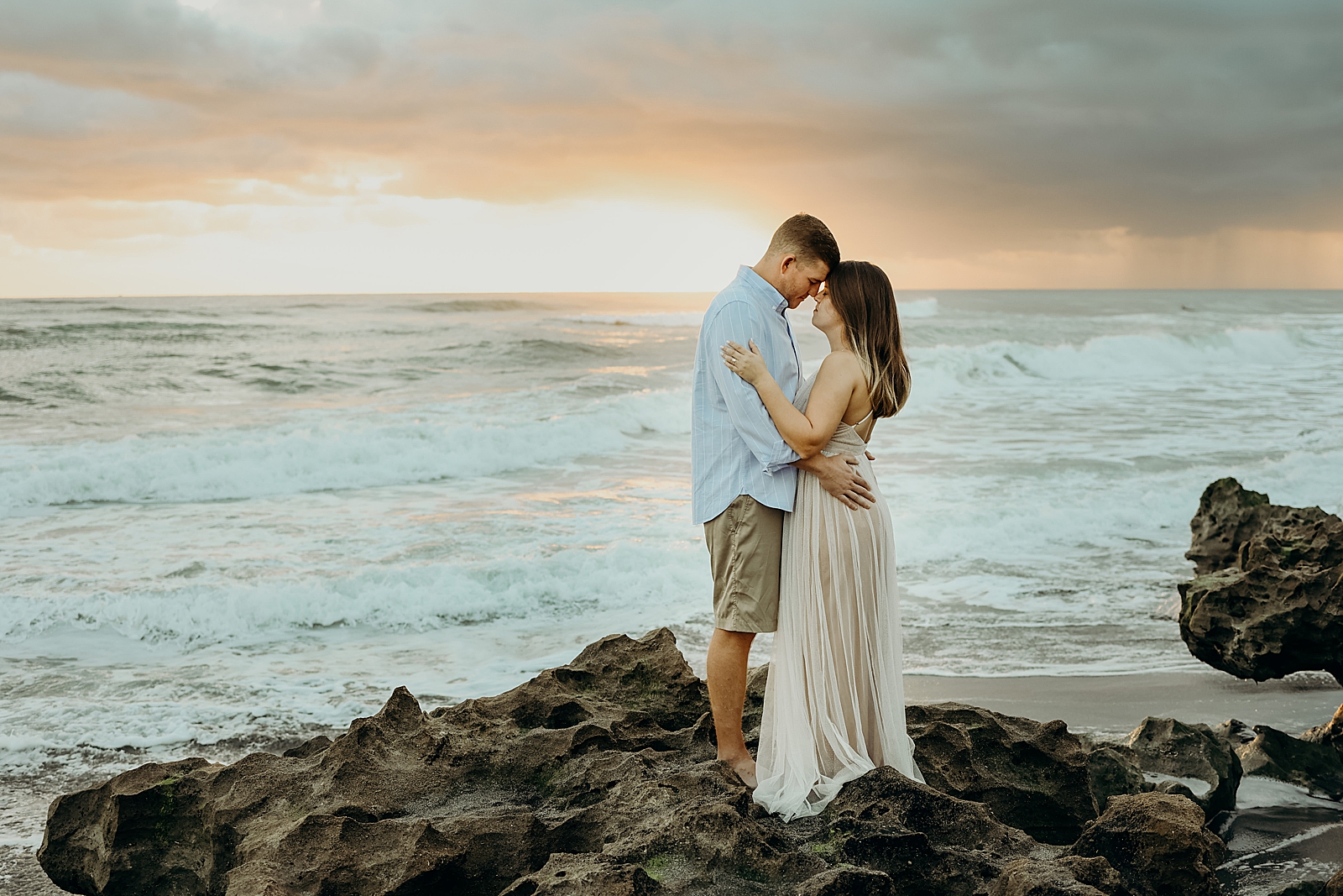 Couple holding each other nuzzling on drift rock on the beach Coral Cove Park Engagement Photography captured by South Florida Family Photographer Maggie Alvarez Photography
