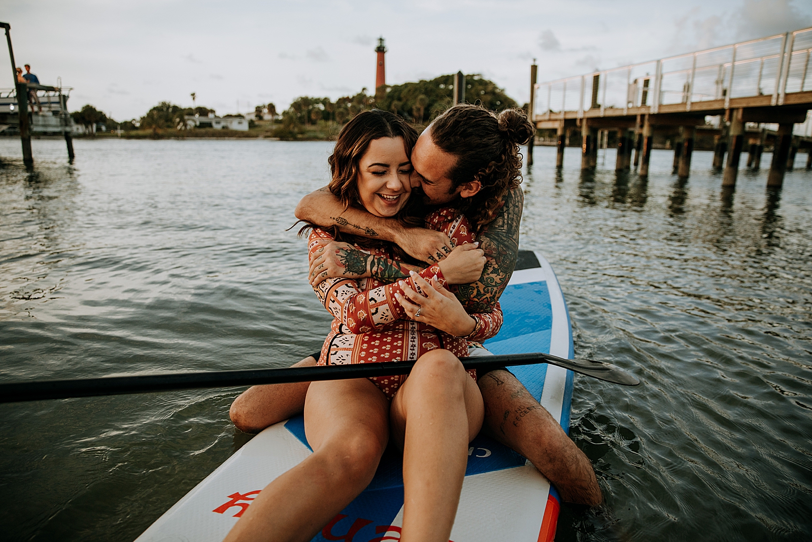 Man wrapping arms around woman on paddle board on calm water Dubois Park Engagement Photography captured by South Florida Family Photographer Maggie Alvarez Photography