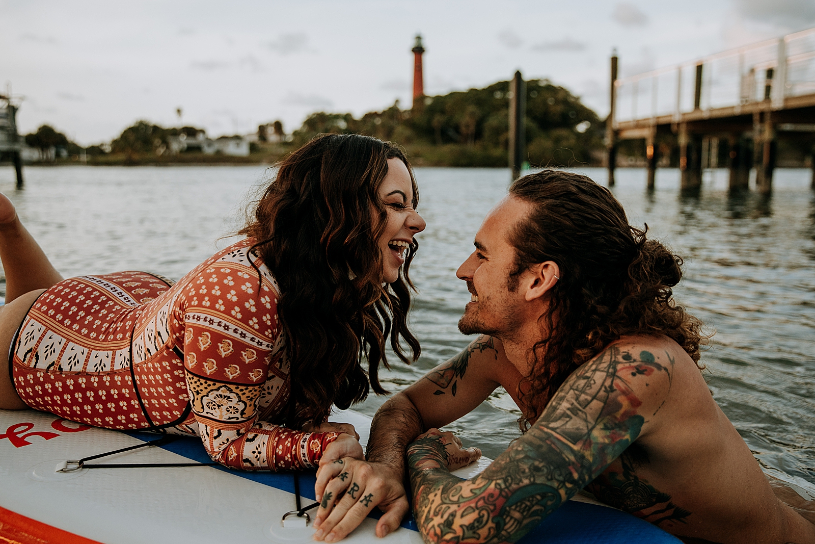 Woman laughing on paddle board with man floating in water holding the paddle board Dubois Park Engagement Photography captured by South Florida Family Photographer Maggie Alvarez Photography