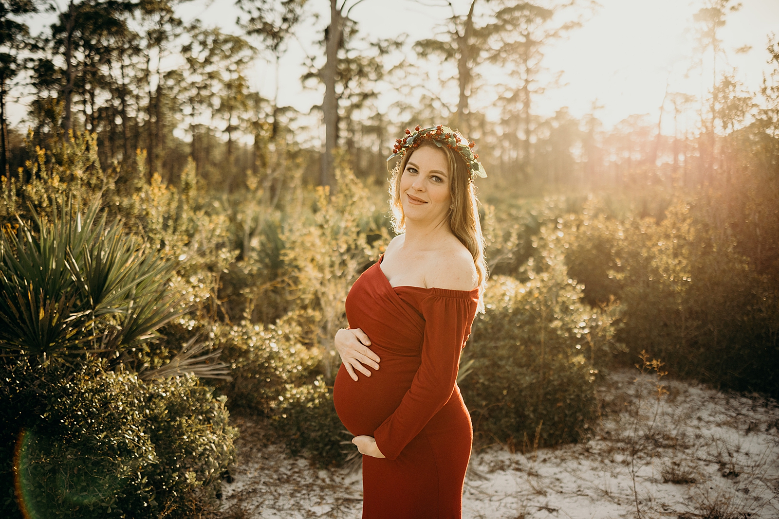Woman holding her pregnant stomach with sun shining on her Johnathan Dickinson Park Maternity Photography captured by South Florida Family Photographer Maggie Alvarez Photography