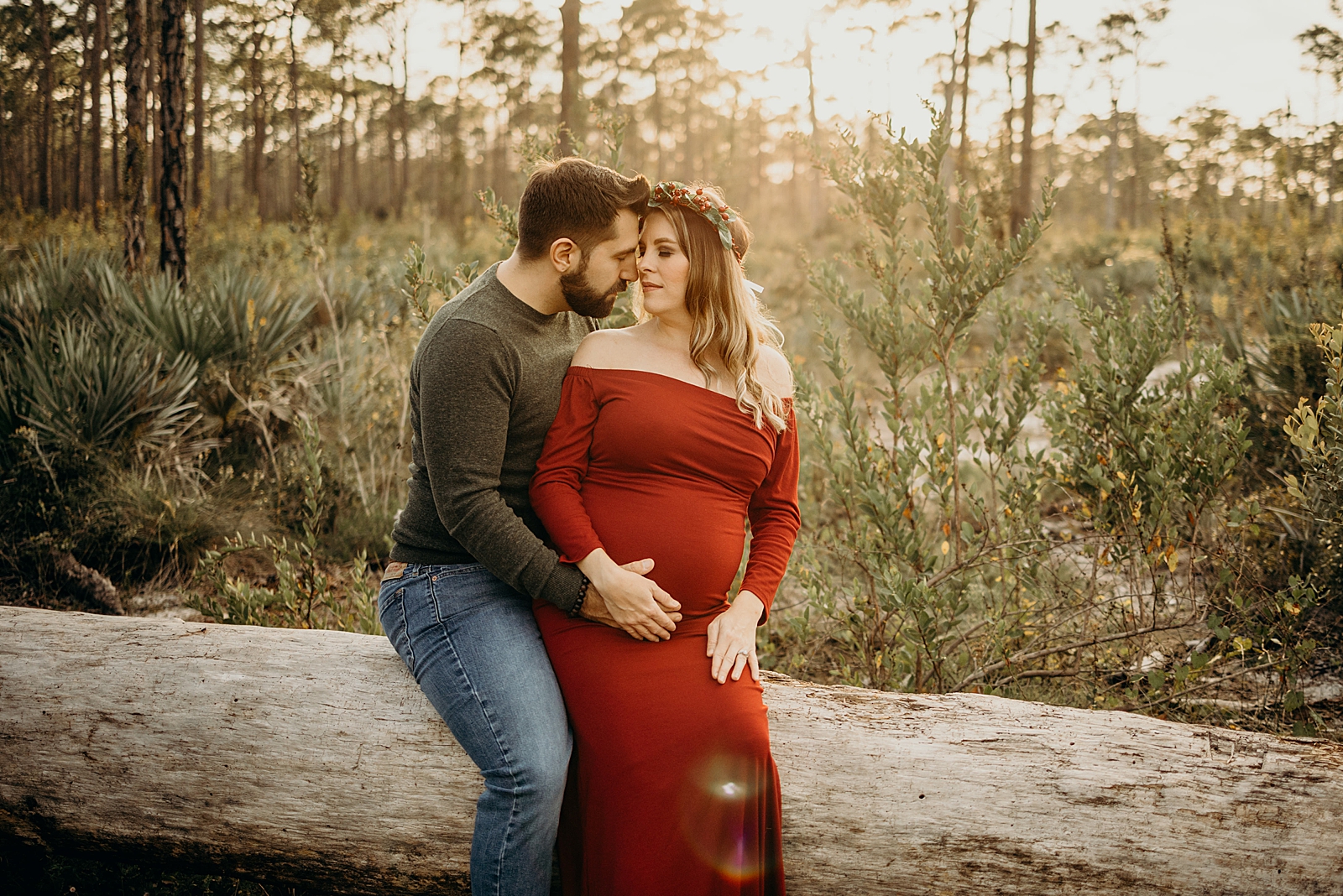 Pregnant husband and wife sitting together on fallen tree Johnathan Dickinson Park Maternity Photography captured by South Florida Family Photographer Maggie Alvarez Photography