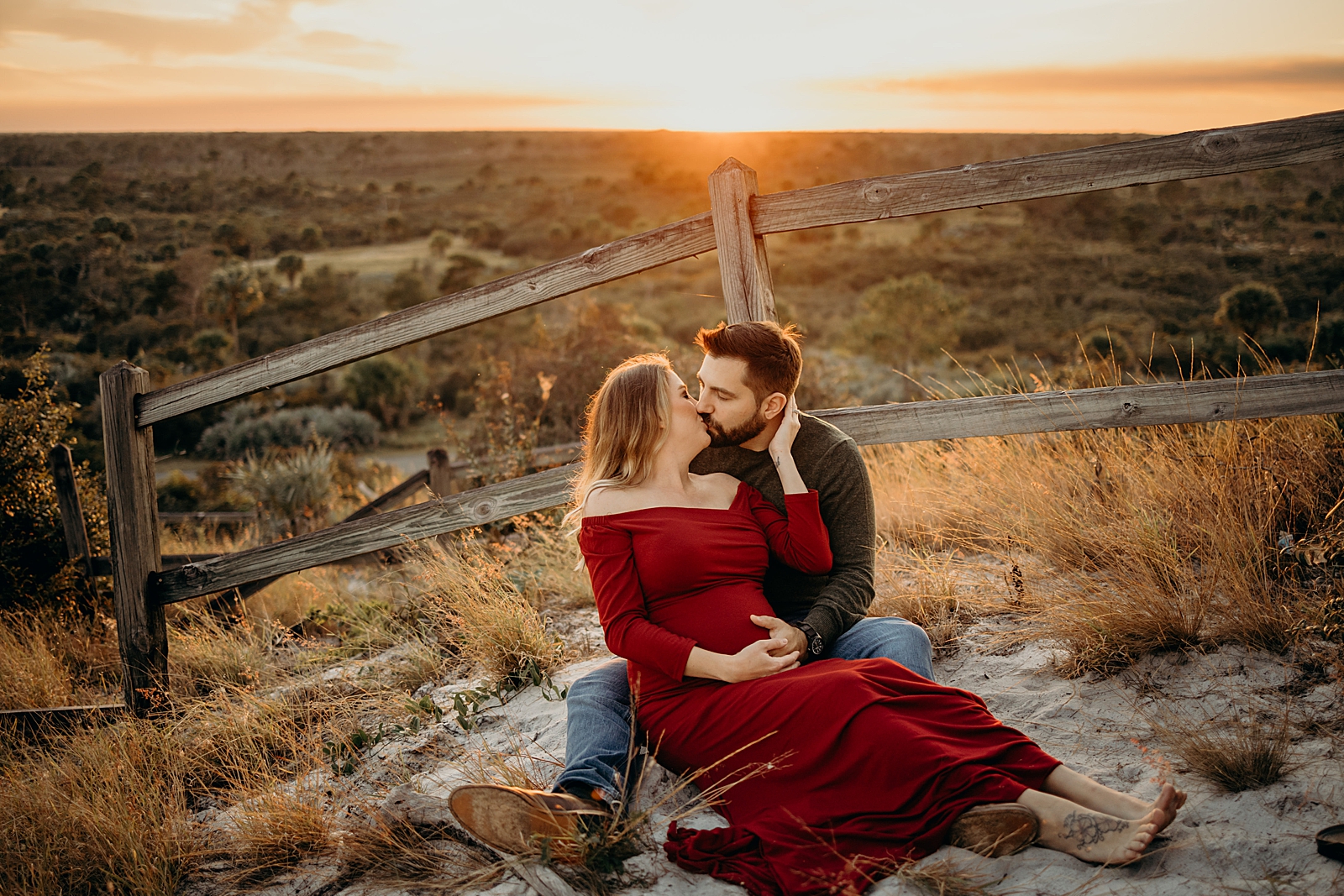 Couple sitting against wood fence with the sun setting Johnathan Dickinson Park Maternity Photography captured by South Florida Family Photographer Maggie Alvarez Photography