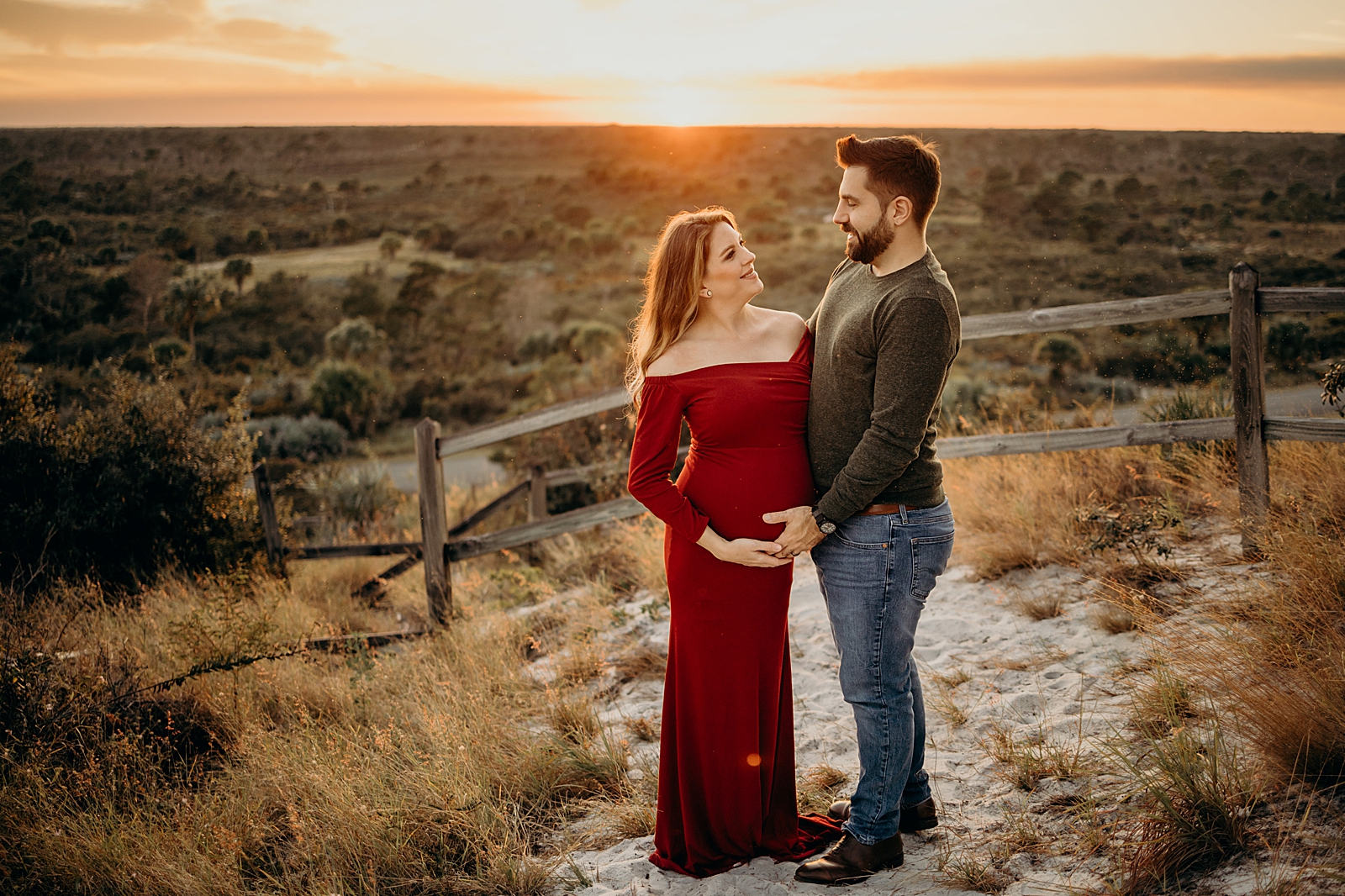 Pregnant couple holding each other standing by wood fence Johnathan Dickinson Park Maternity Photography captured by South Florida Family Photographer Maggie Alvarez Photography