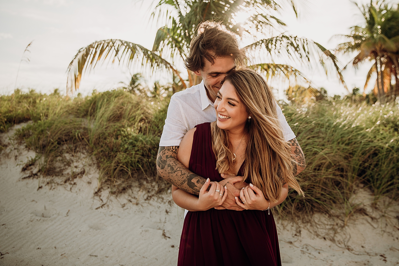Man wrapping arms around woman on the sand Key Biscayne Beach Engagement Photography captured by South Florida Family Photographer Maggie Alvarez Photography