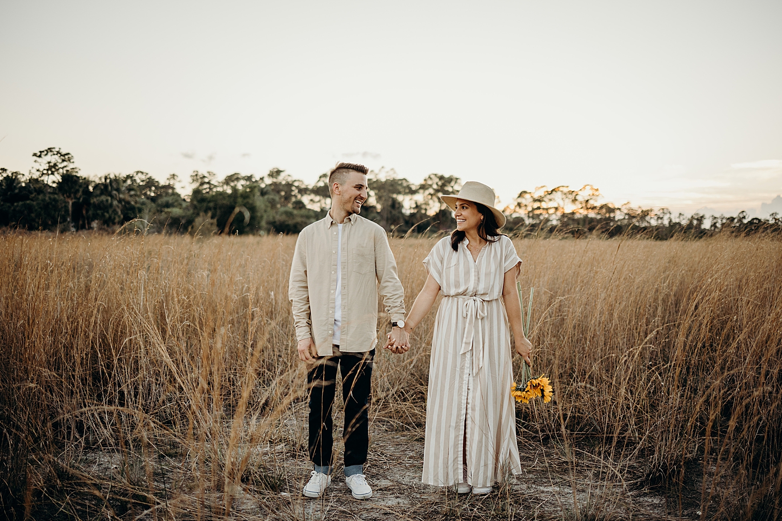 Couple holding hands and lady holding sunflowers Royal Palm Nature Preserve Engagement Photography captured by South Florida Engagement Photographer Maggie Alvarez Photography