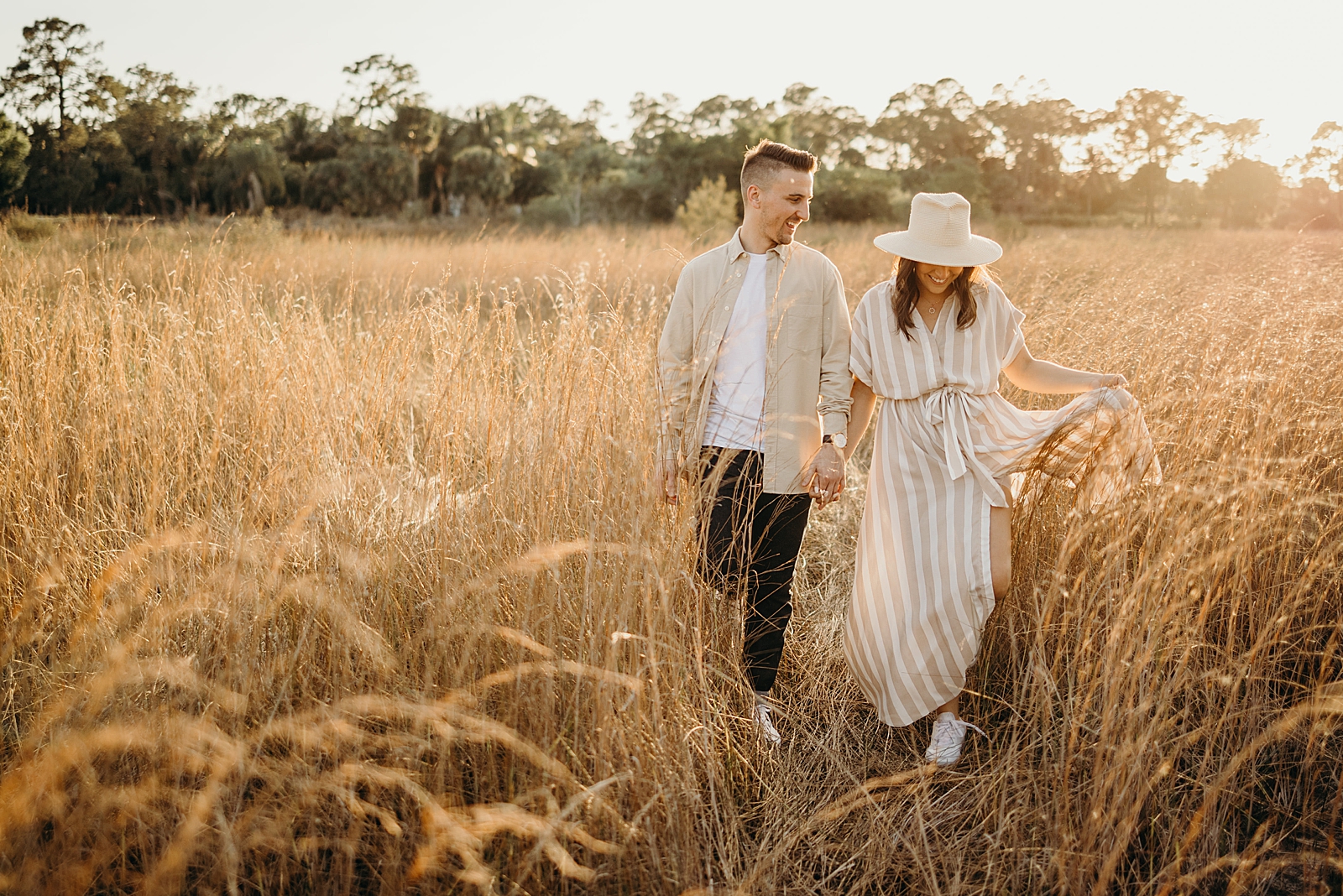 Couple walking through tall grain field holding hands Royal Palm Nature Preserve Engagement Photography captured by South Florida Engagement Photographer Maggie Alvarez Photography