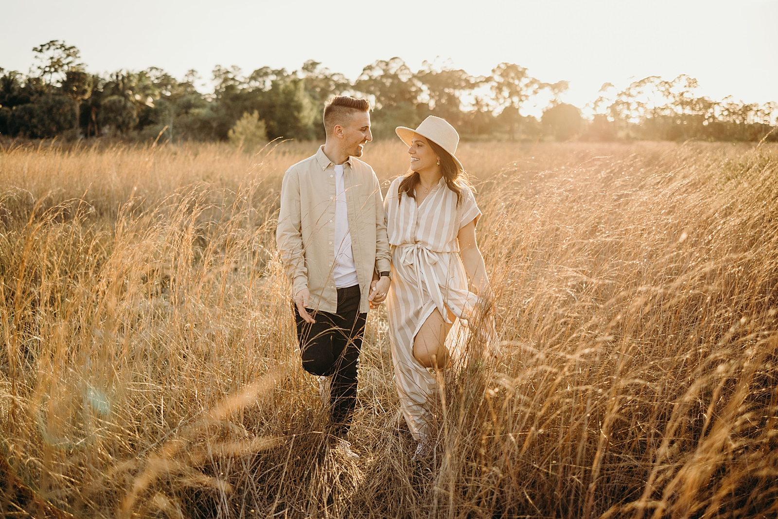 Couple holding hands walking through tall dried grass field Royal Palm Nature Preserve Engagement Photography captured by South Florida Engagement Photographer Maggie Alvarez Photography