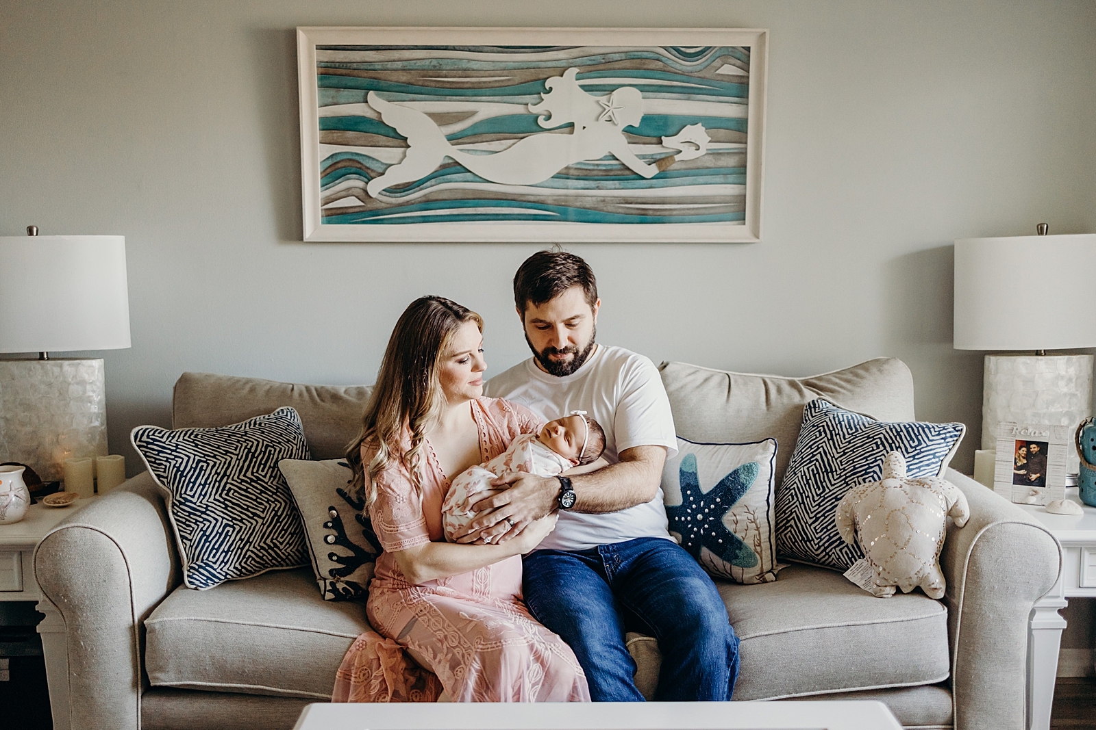 Parents sitting on the couch with oceanic pillows holding newborn baby girl South Florida Newborn Photography Photography captured by South Florida Family Photographer Maggie Alvarez Photography