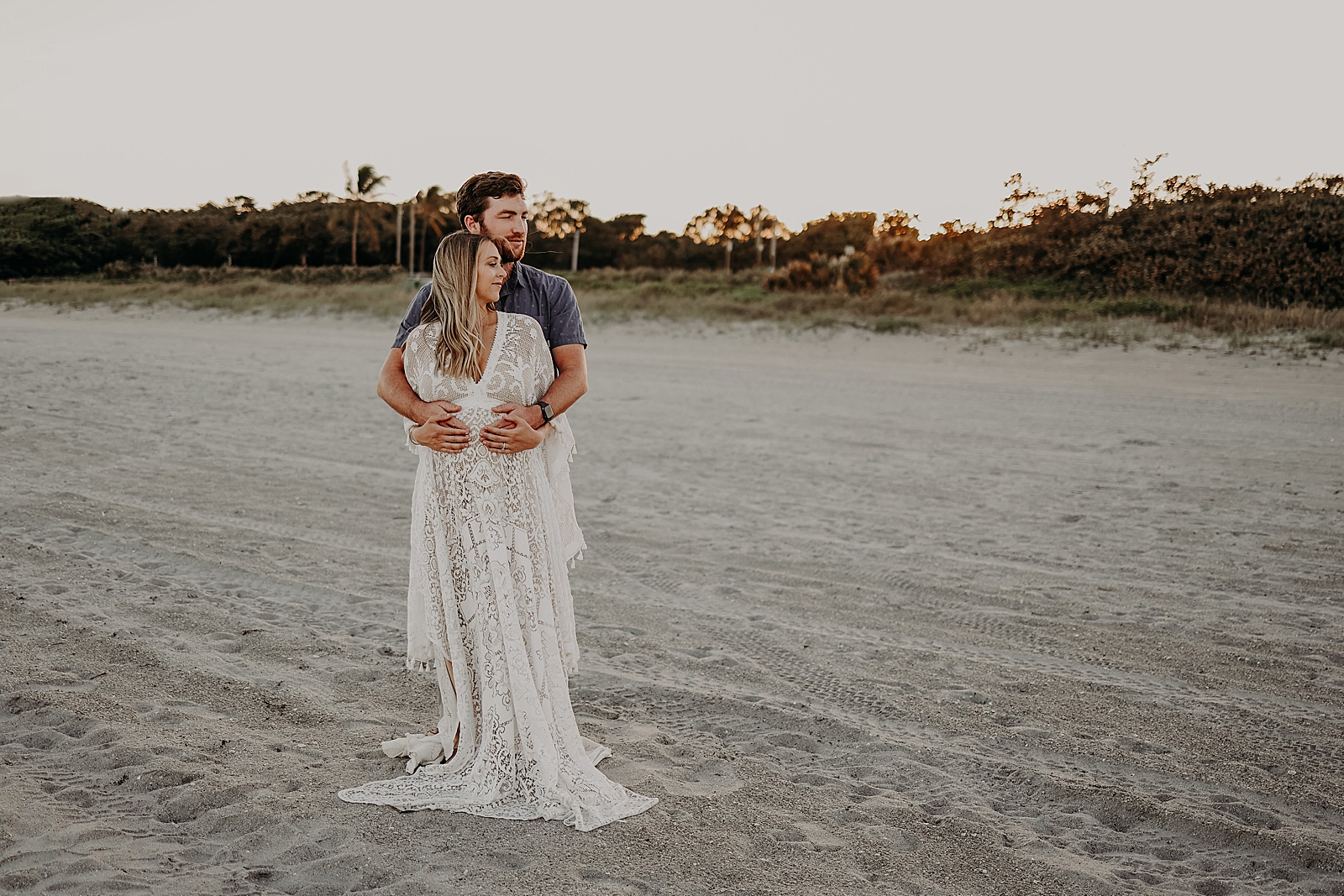 Man holding baby bump from behind on the sand Spanish River Park Maternity Photography captured by South Florida Family Photographer Maggie Alvarez Photography