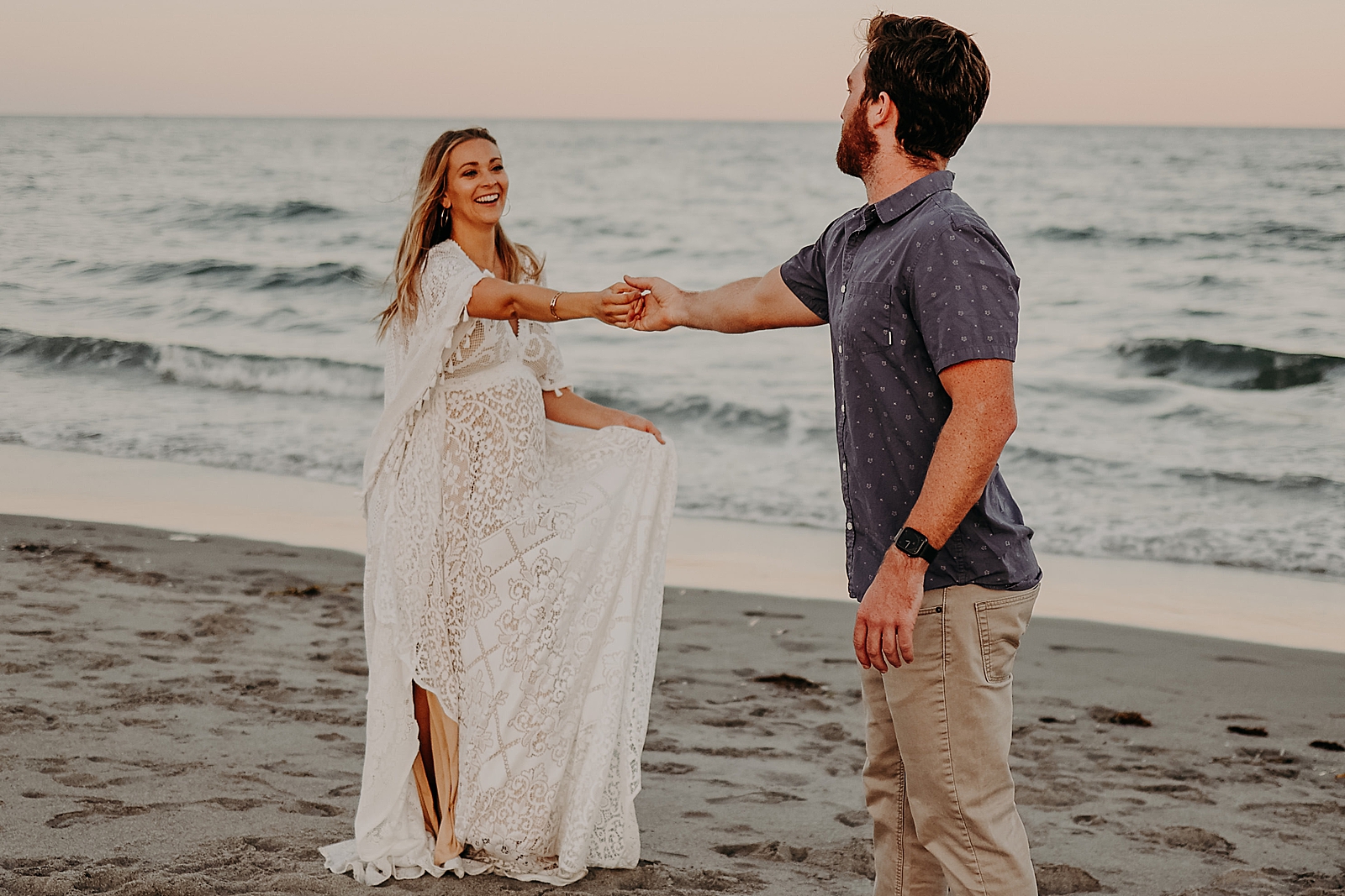 Couple extending their arms to each other to hold their hands in front of the ocean Spanish River Park Maternity Photography captured by South Florida Family Photographer Maggie Alvarez Photography