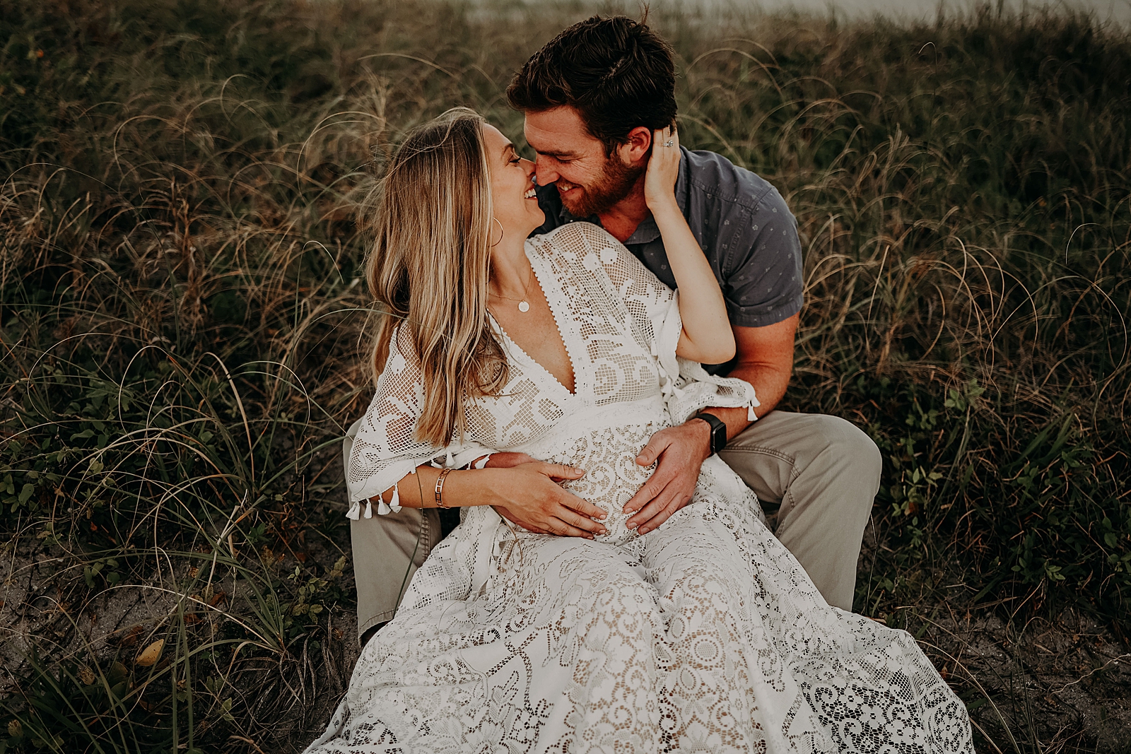 Husband sitting holding pregnant wife Spanish River Park Maternity Photography captured by South Florida Family Photographer Maggie Alvarez Photography