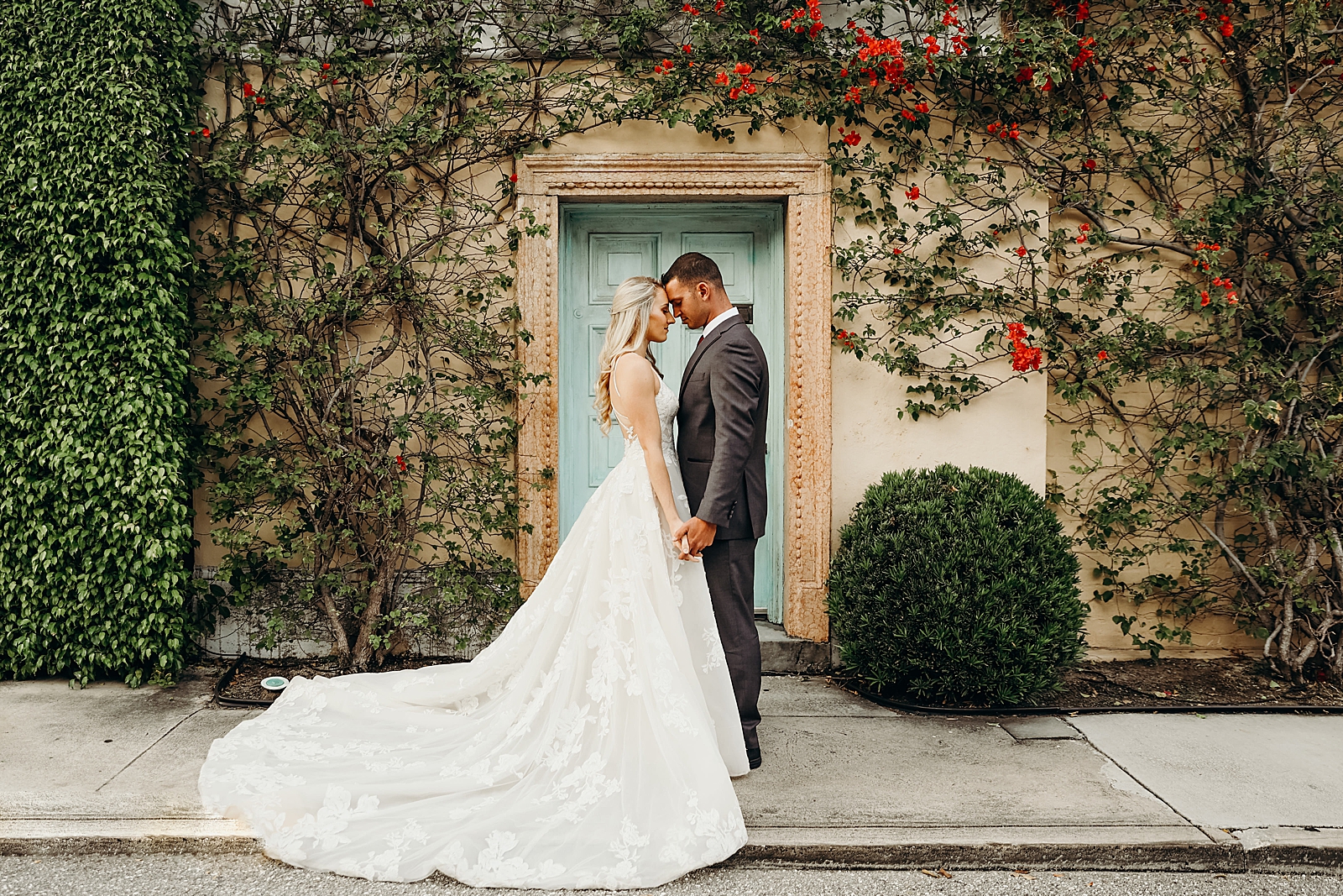 Couple holding hands and resting their foreheads against each others in front of turquoise door Worth Avenue Bridal Photography captured by South Florida Engagement Photographer Maggie Alvarez Photography
