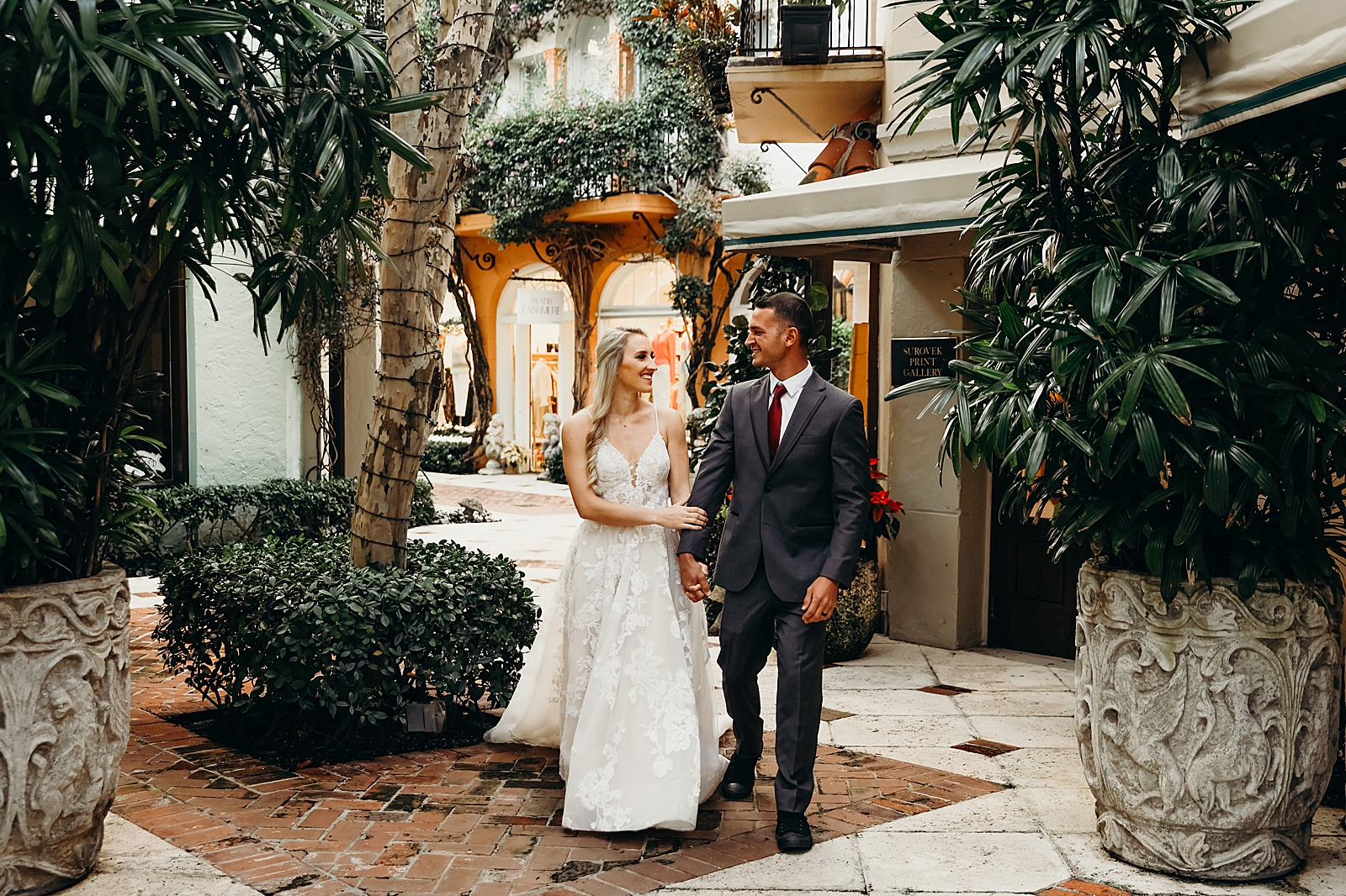 Couple holding hands strolling through courtyard Worth Avenue Bridal Photography captured by South Florida Engagement Photographer Maggie Alvarez Photography