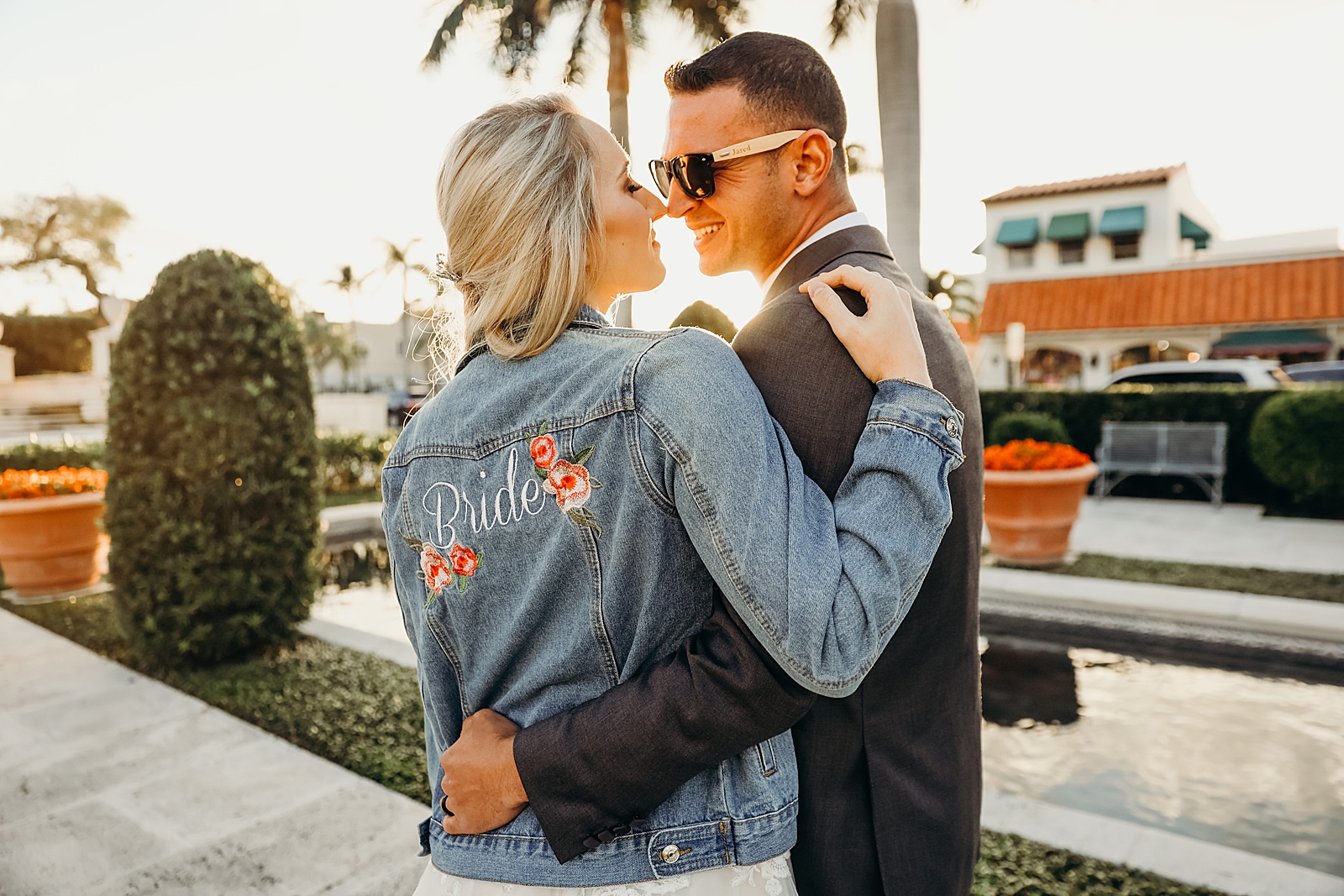 Couple about to kiss with man in sunglasses and woman wearing Bride jean jacket Worth Avenue Bridal Photography captured by South Florida Engagement Photographer Maggie Alvarez Photography