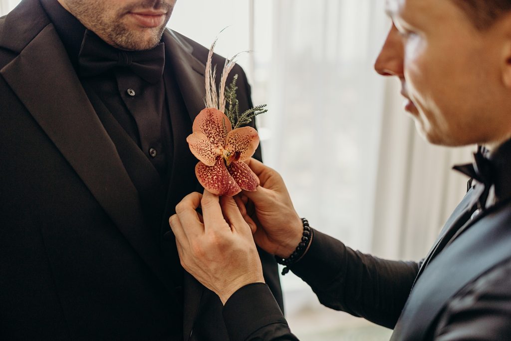 Groom Getting ready getting red tropical boutonniere put on 