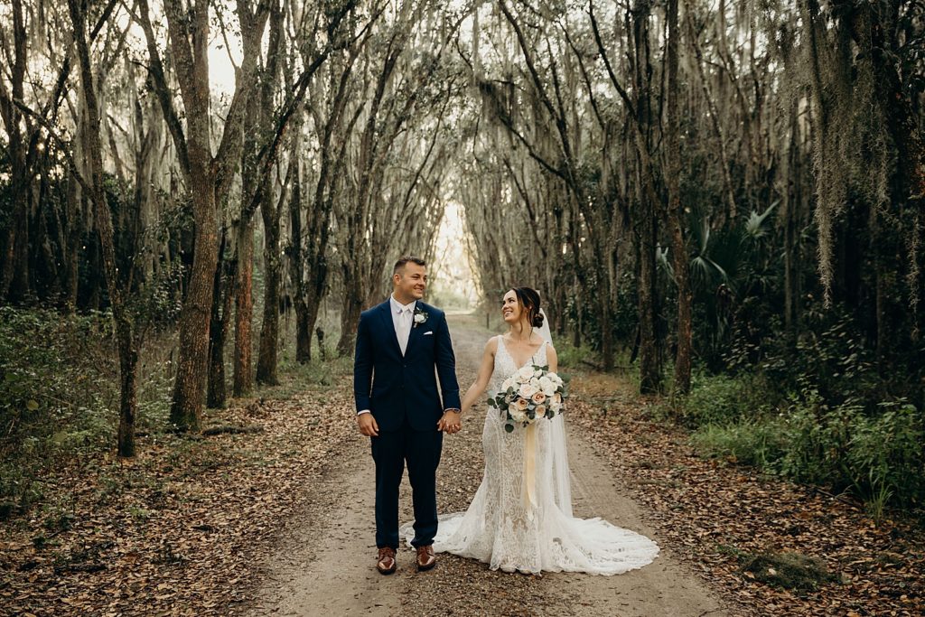 Bride and Groom holding hands standing on forest path with trees surrounding them