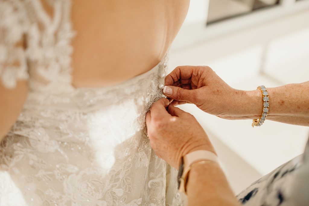 Closeup of Mother buttoning Bride's dress