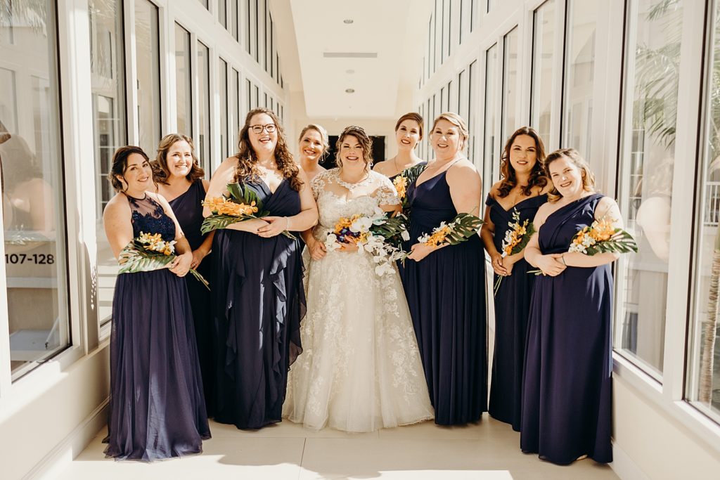Bride with Bridesmaids with bouquets in glass window hallway