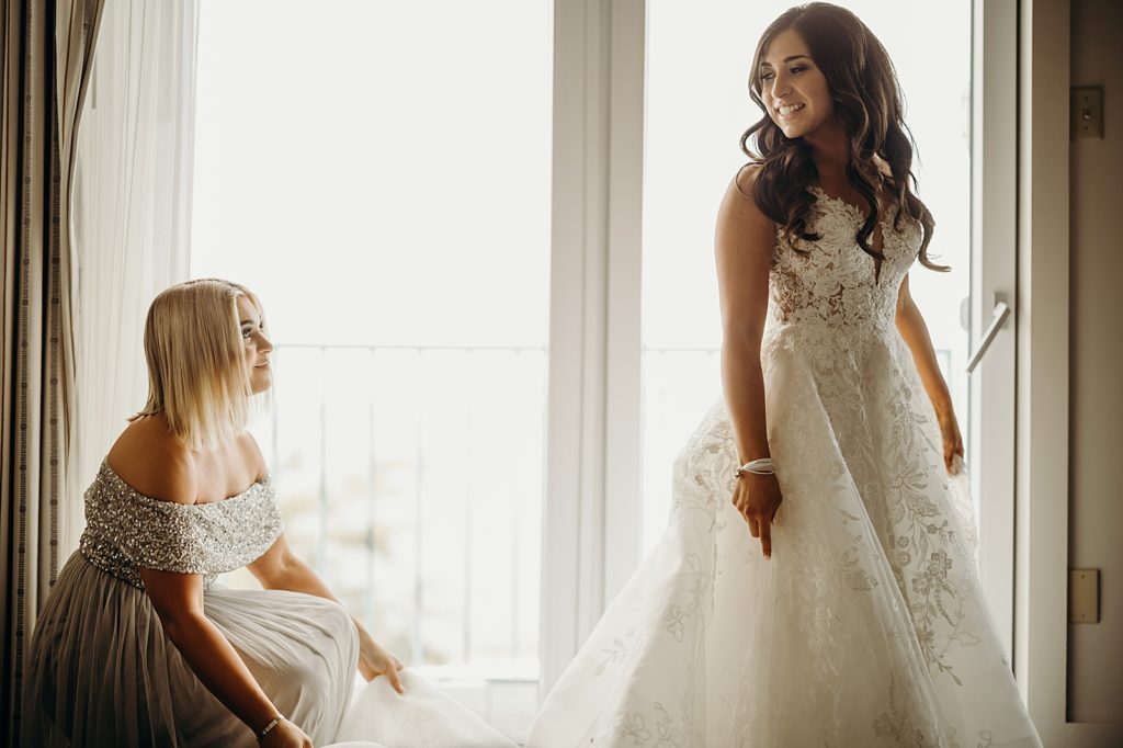 Bridesmaid helping Bride a=extend wedding dress train by the window