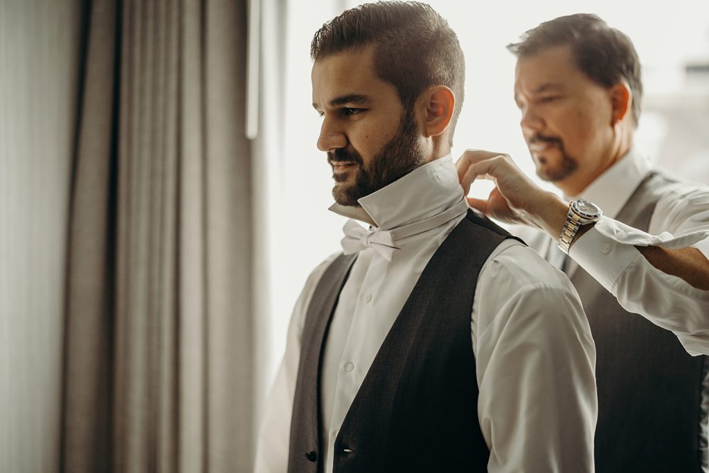 Groom getting help getting ready putting on bow tie