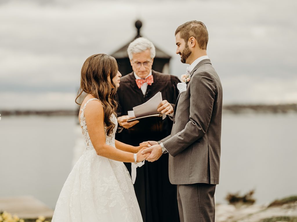 Bride and Groom hand in hand during Officiant's Homily for outdoor waterside Ceremony
